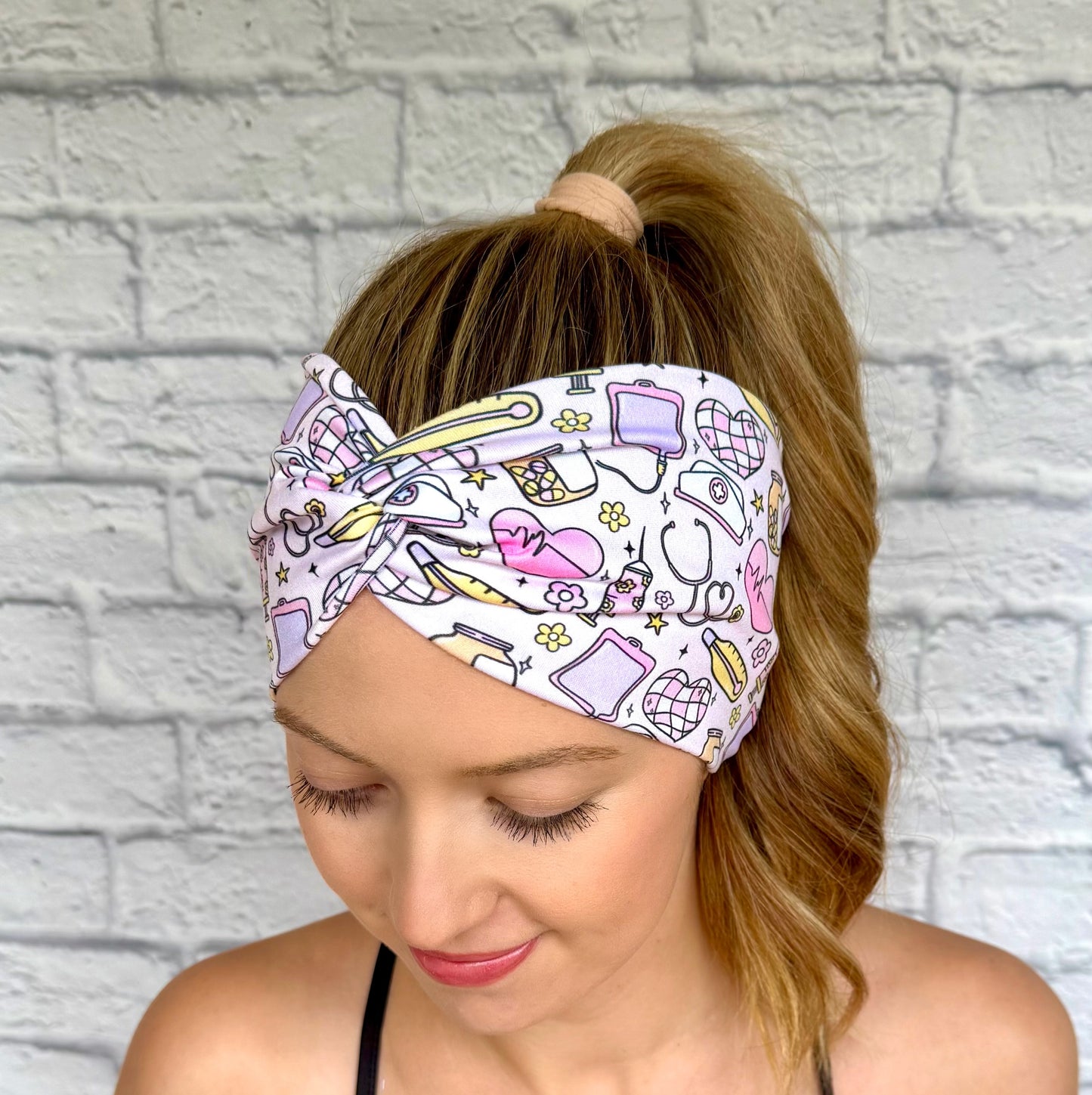 Woman with hair in ponytail wearing wide, twisted headband with yellow, purple, and pink disco and medical theme print.