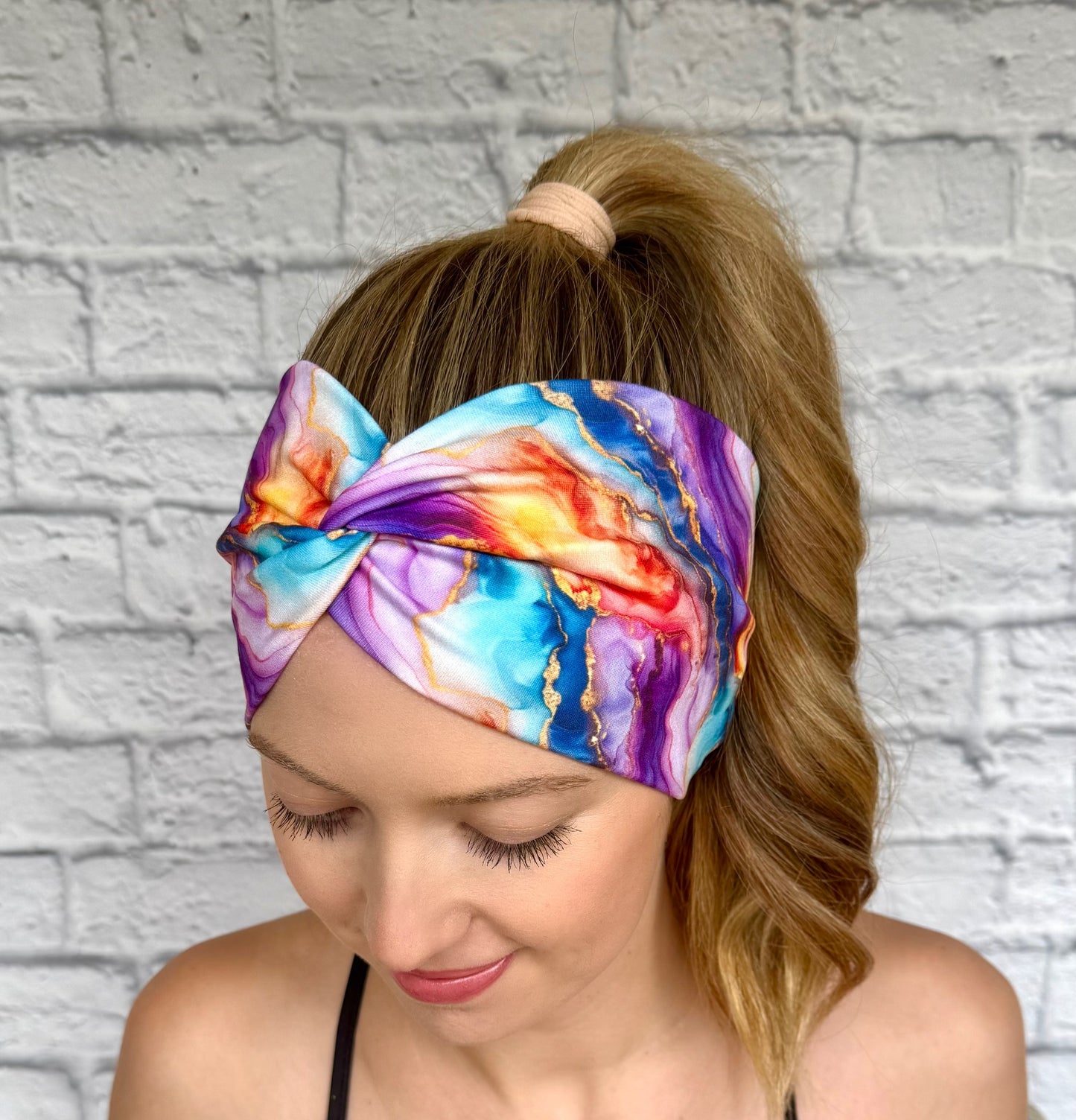 Woman with hair in ponytail wearing wide, twisted headband in multi-color watercolor print.
