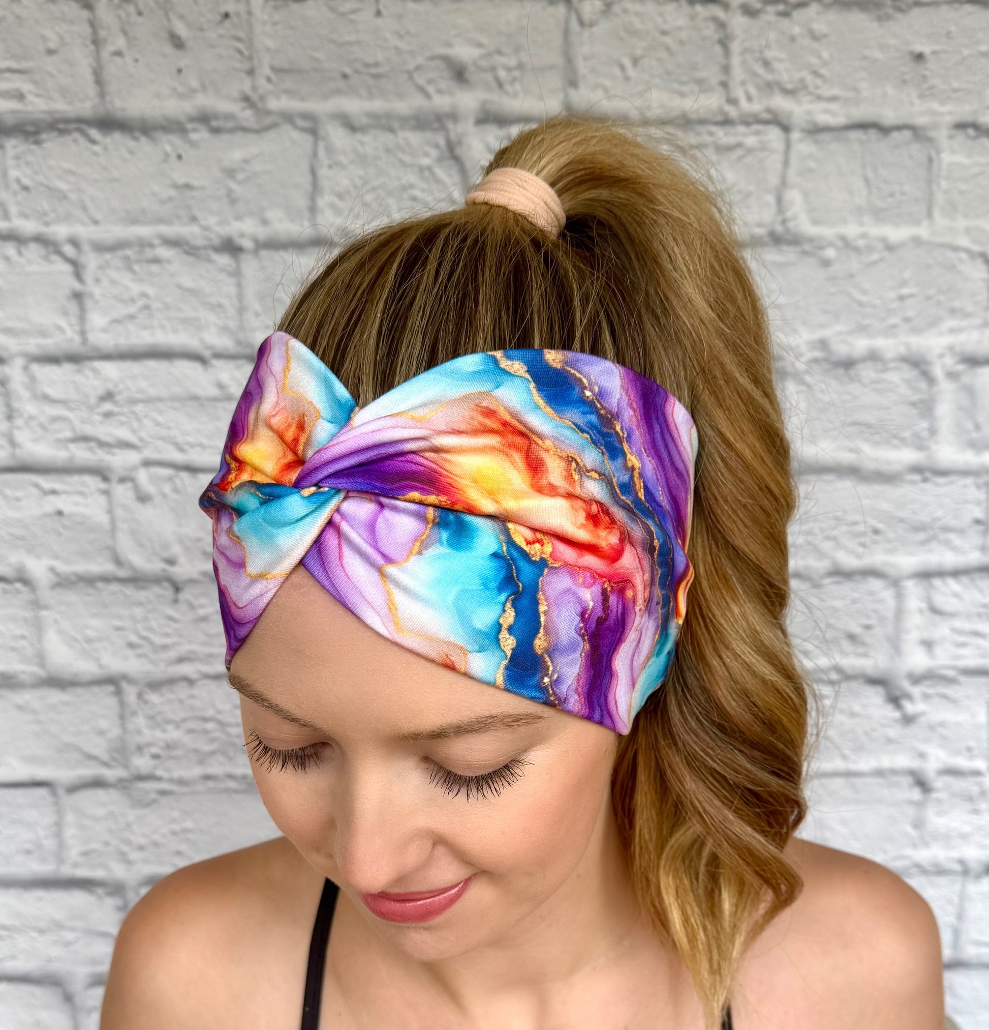Woman with hair in ponytail wearing wide, twisted headband in multi-color watercolor print.
