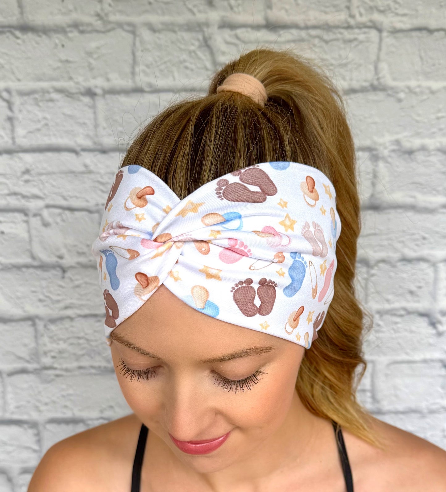 Woman with hair in ponytail wearing wide, twisted, white headband with baby feet and baby theme print.