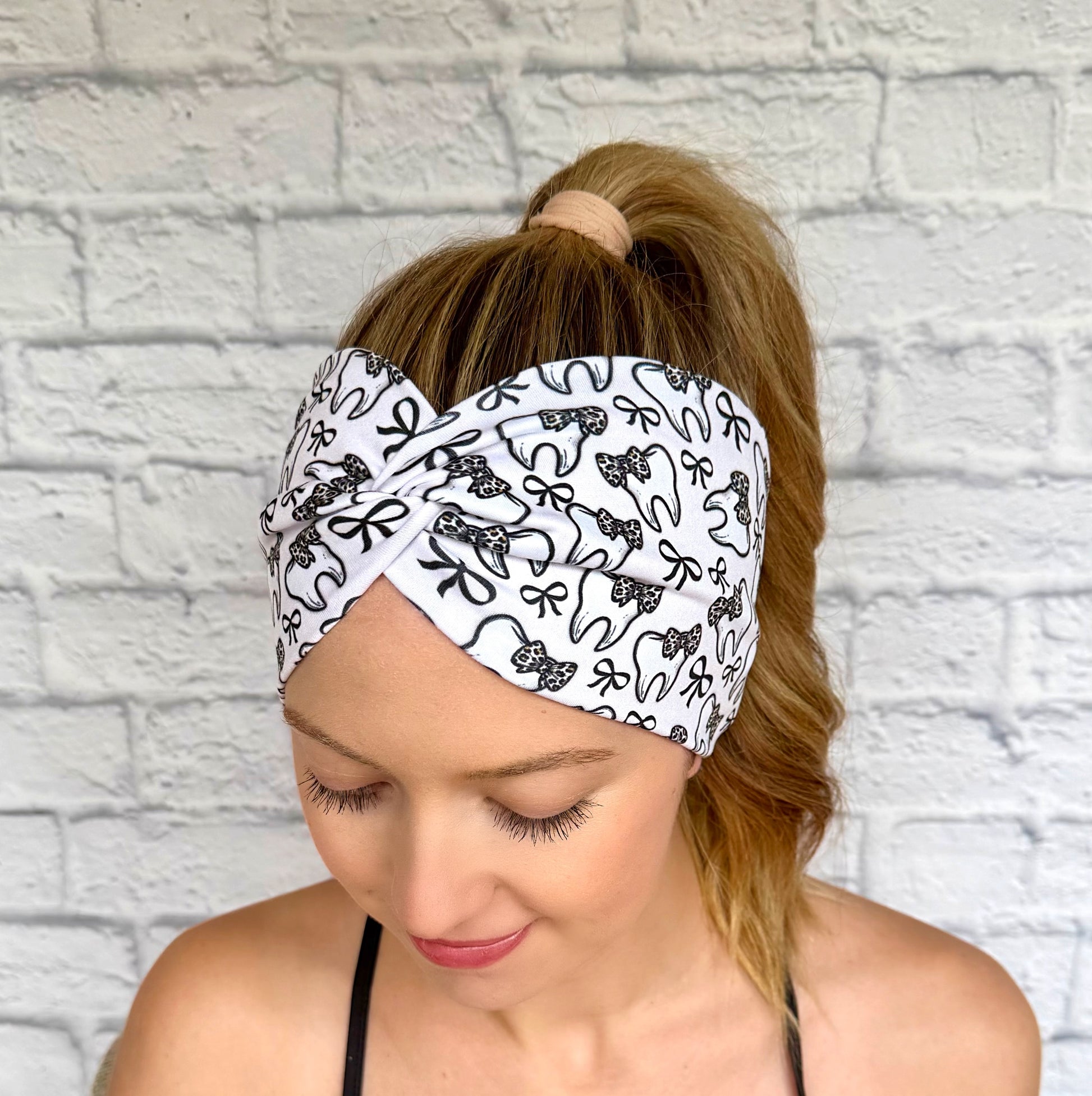 Woman with hair in curled ponytail wearing wide, twisted, white headband in white with teeth and bow print in black and cheetah print.