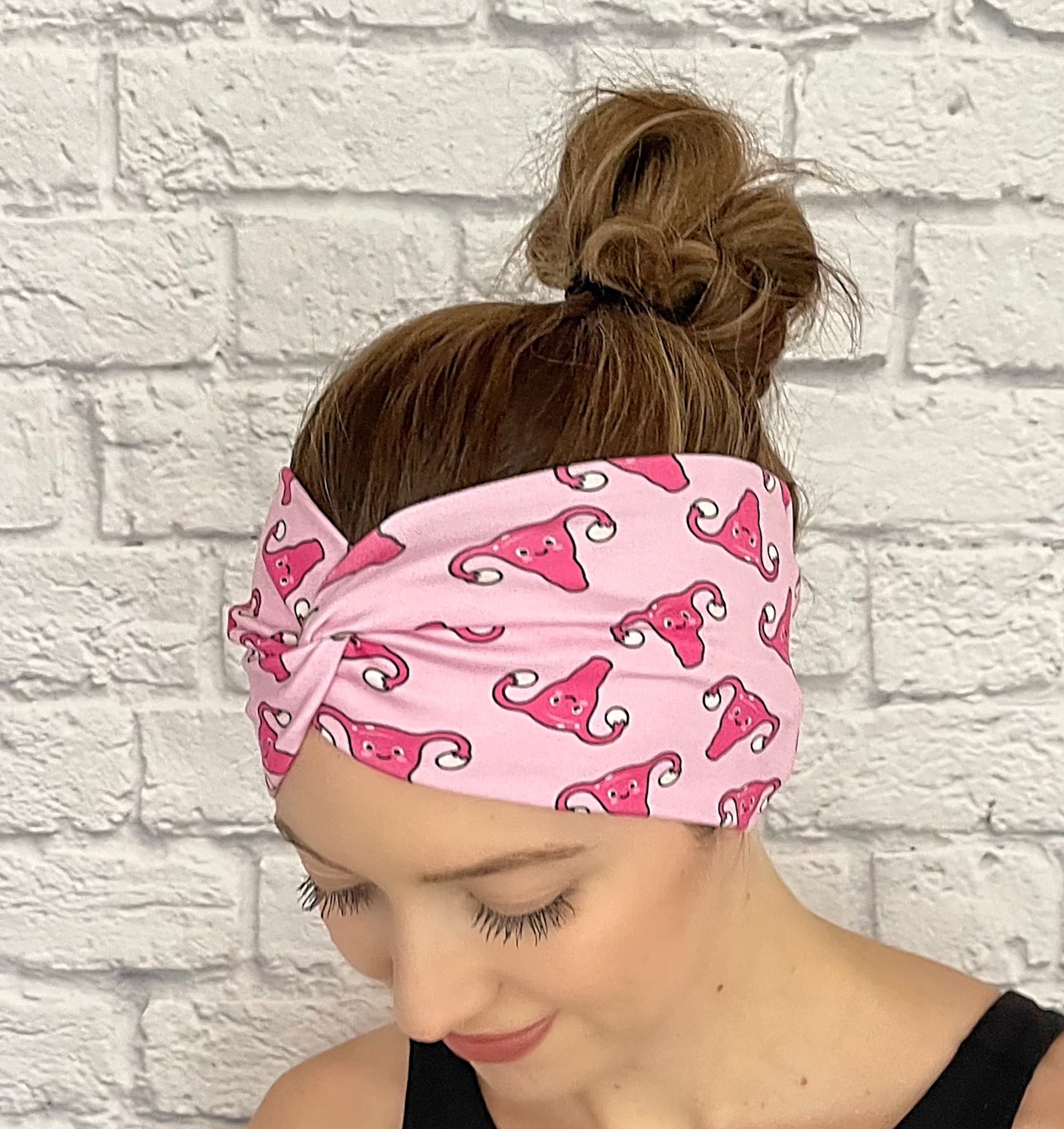 Woman with hair in bun wearing wide, twisted headband in light pink with dark pink uterus print.