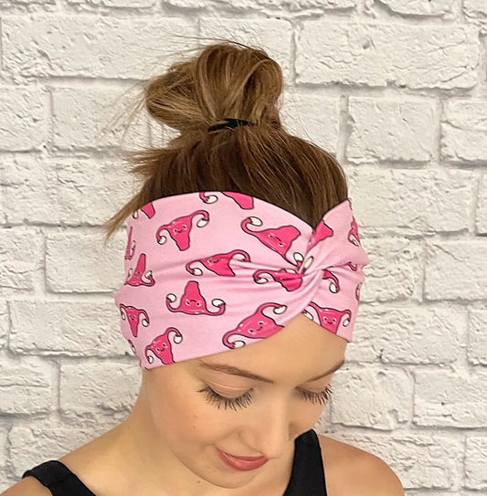 Woman with hair in bun wearing wide, twisted headband in light pink with dark pink uterus print.
