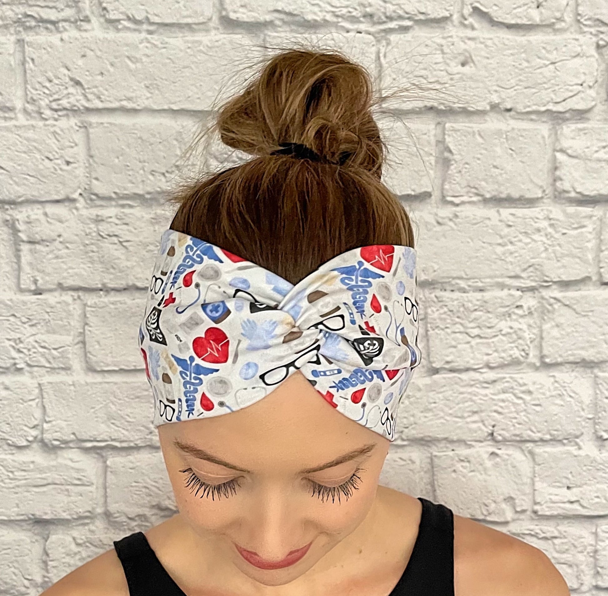 Woman with hair in bun wearing wide, twisted headband in light blue, red, and black medical theme print.