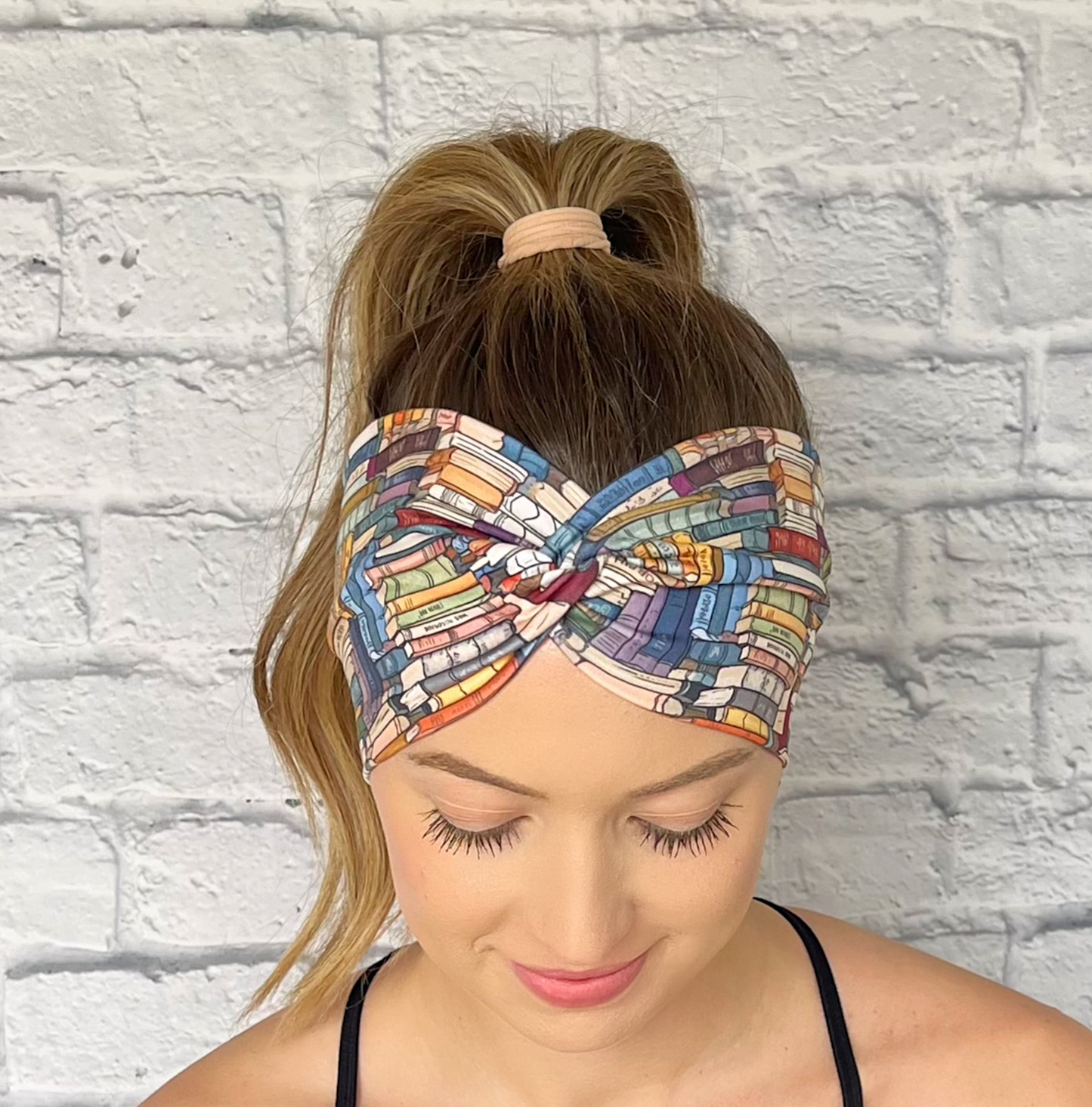 Woman with hair in curled ponytail wearing wide, twisted headband with book print.