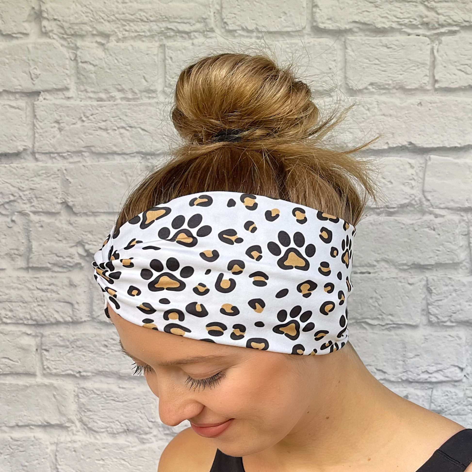 Woman with hair in bun wearing wide, white, twisted headband with brown and black dog paws and cheetah print.