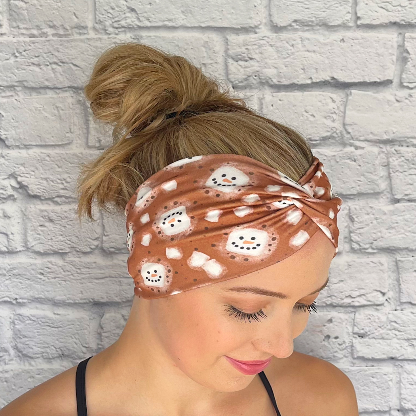 Woman with hair in bun wearing brown, wide, twisted headband with white snowman hot chocolate print.