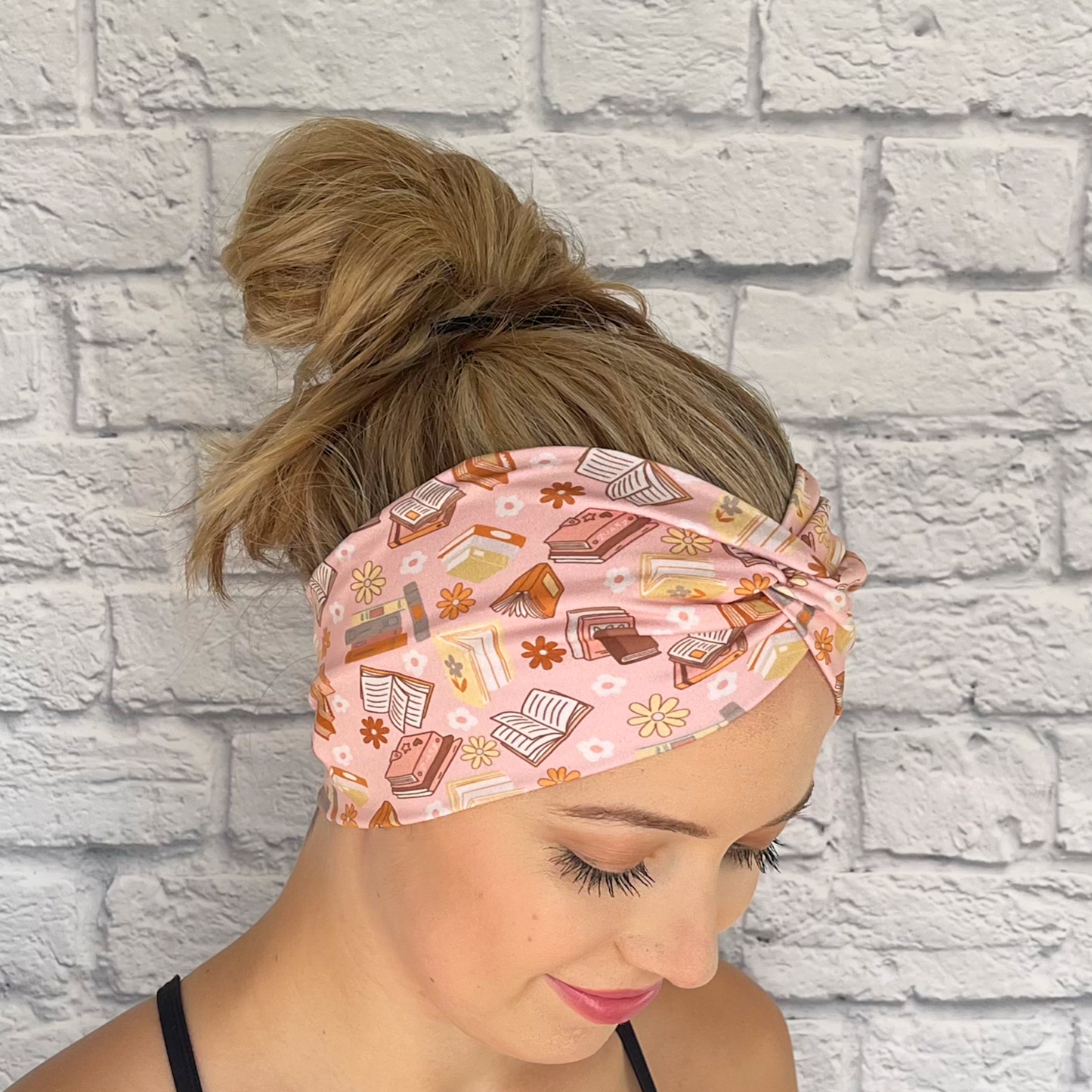 Woman wearing pink, wide twisted headband with books and flower print.