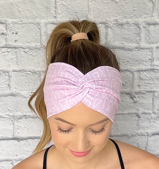 Woman with hair in curled ponytail wearing wide, twisted headband in light pink with white teeth print.