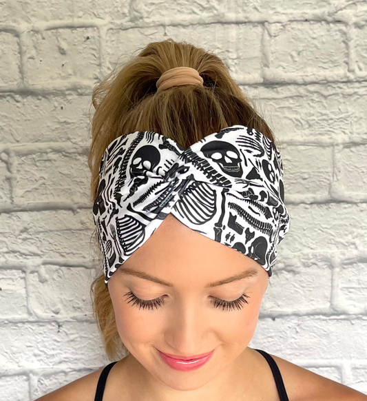 Woman with hair in curled ponytail wearing white, wide twist headband with black skeleton print.
