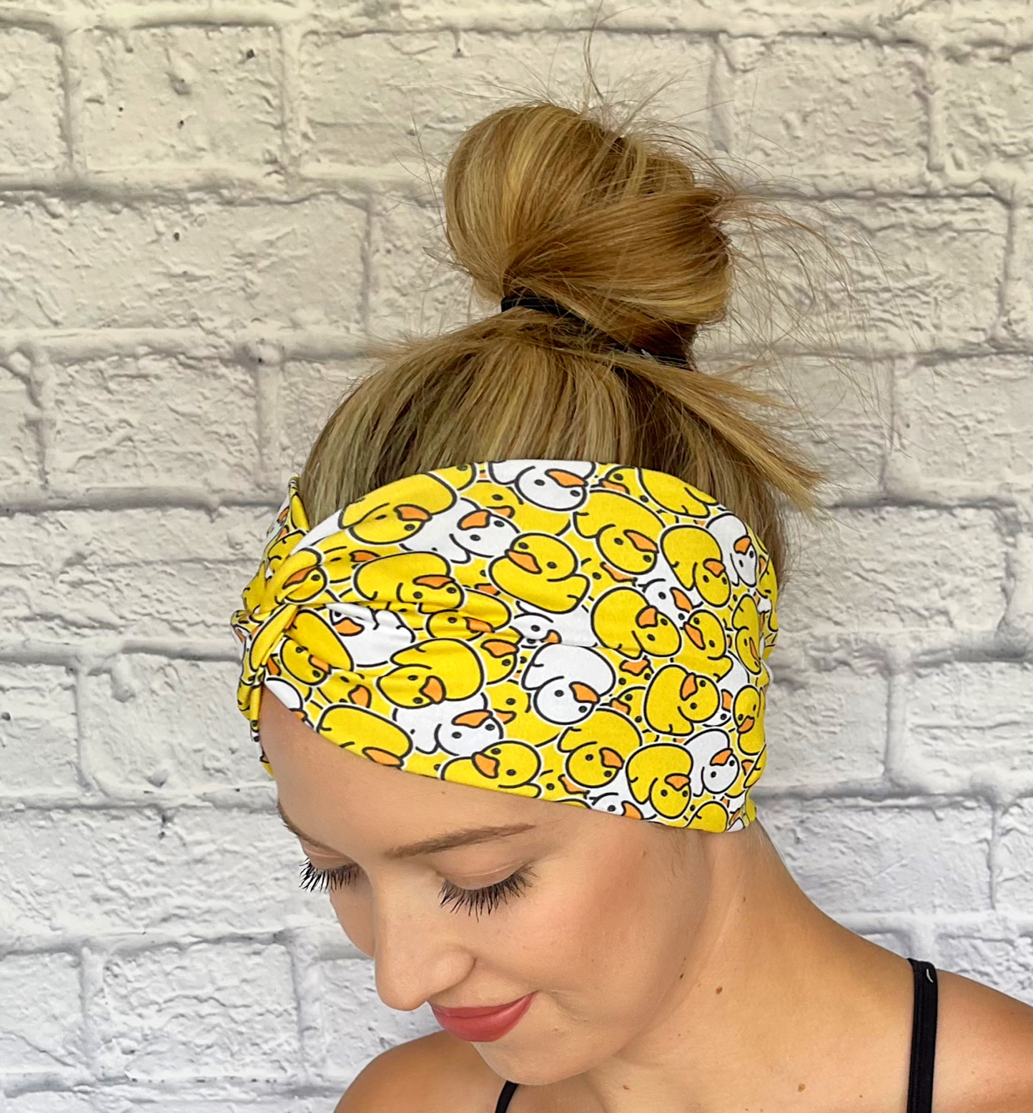 Woman with hair in bun wearing wide, twisted headband in yellow and white rubber duck print.