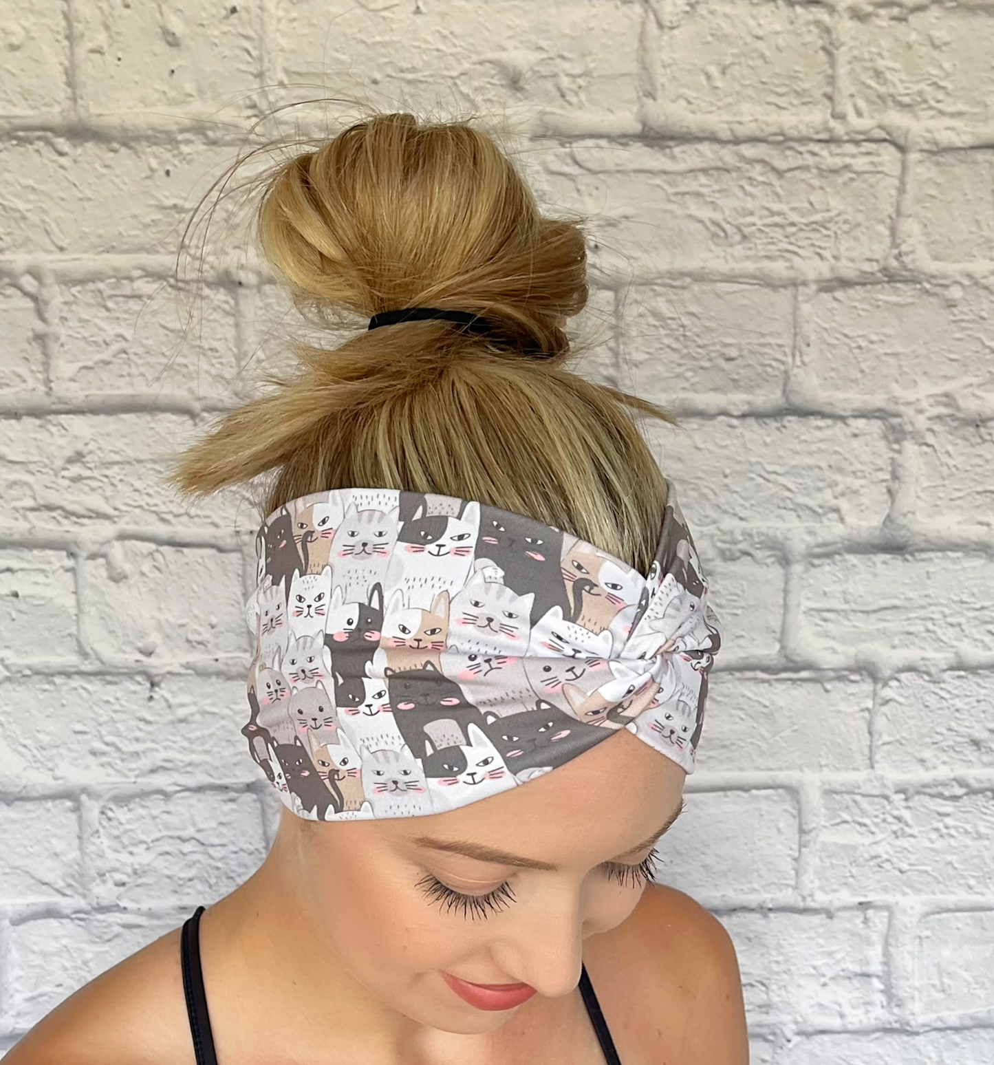 Woman with hair in bun wearing wide, twisted headband in with gray and tan cat print.
