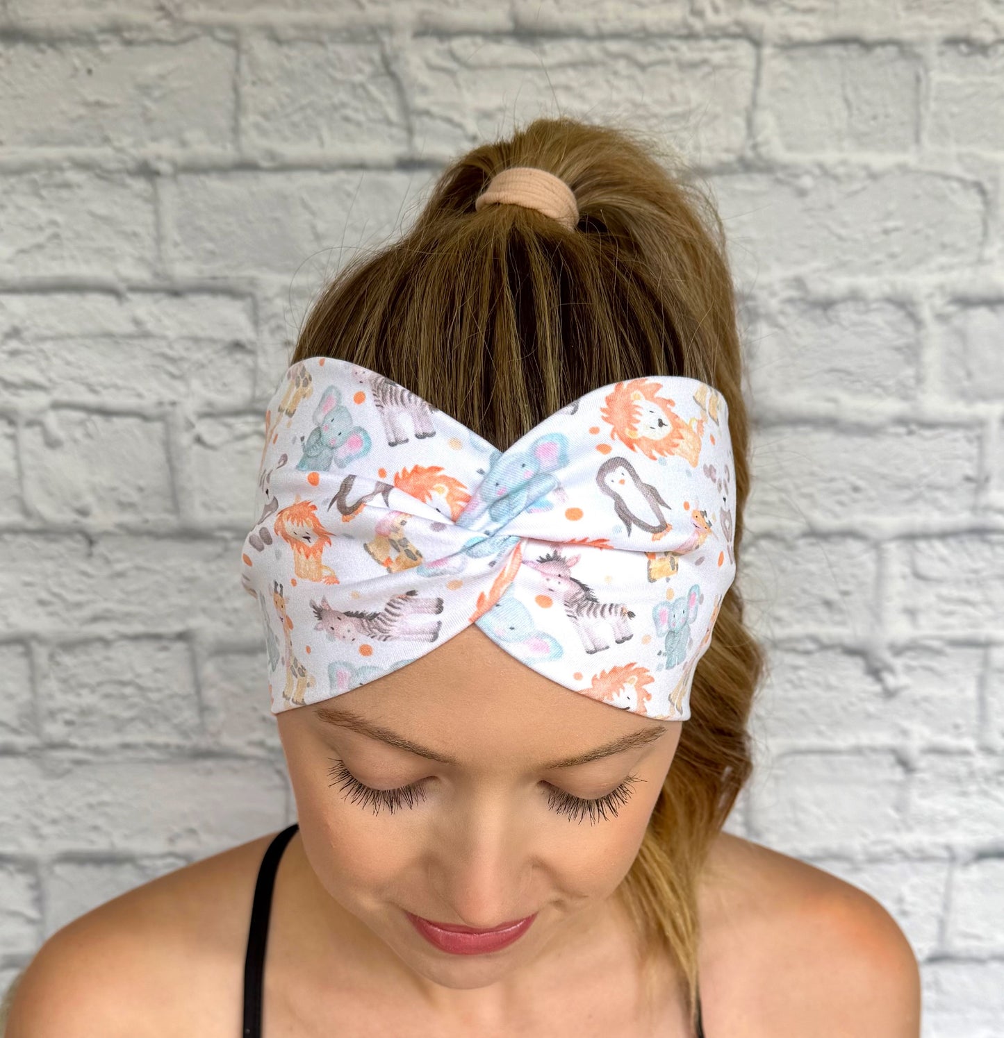 Woman with hair in ponytail wearing wide, twisted headband in white with baby animal and polka dot print.