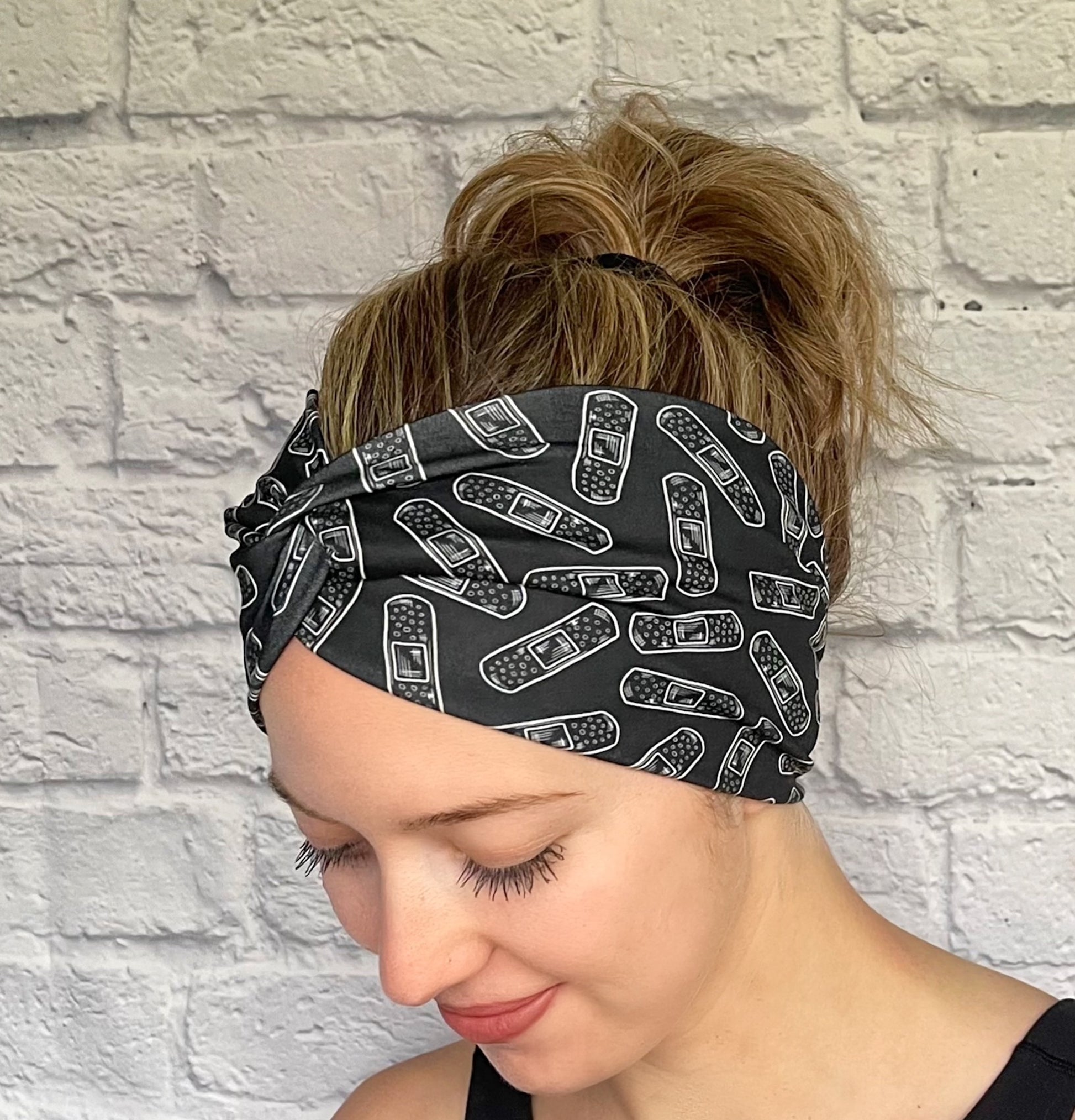 Woman with hair in bun wearing wide, twisted headband in black with white bandage print.