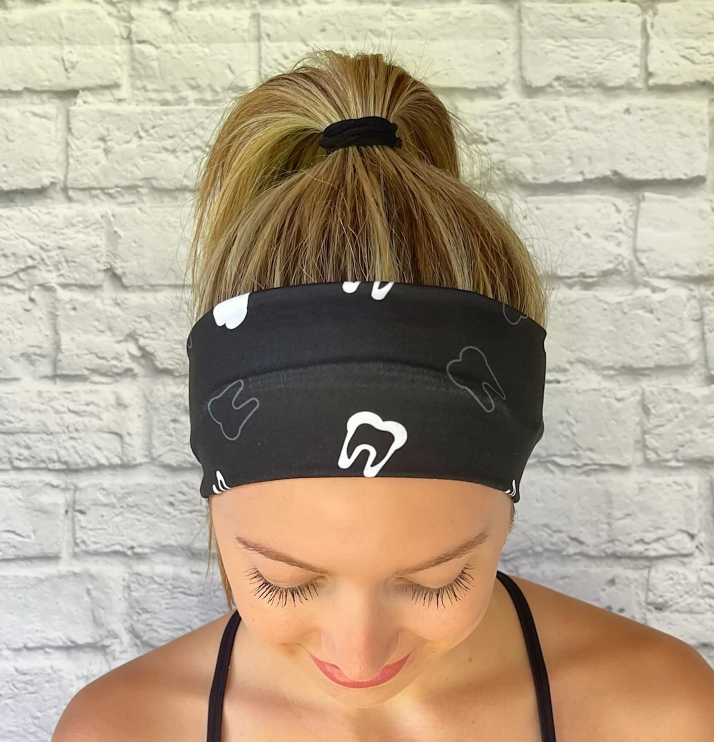Woman with hair in ponytail wearing flat, stretchy, black headband with white teeth print.