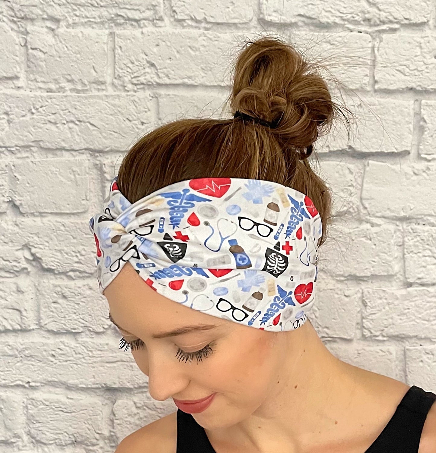 Woman with hair in bun wearing wide, twisted headband in light blue, red, and black medical theme print.