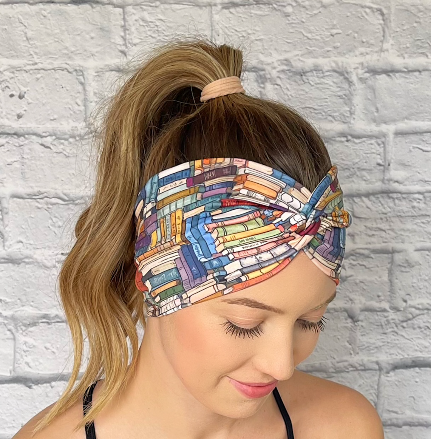 Woman with hair in curled ponytail wearing wide, twisted headband with book print.