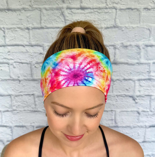 Woman with hair in ponytail wearing flat, stretchy headband in rainbow color tie dye pattern.