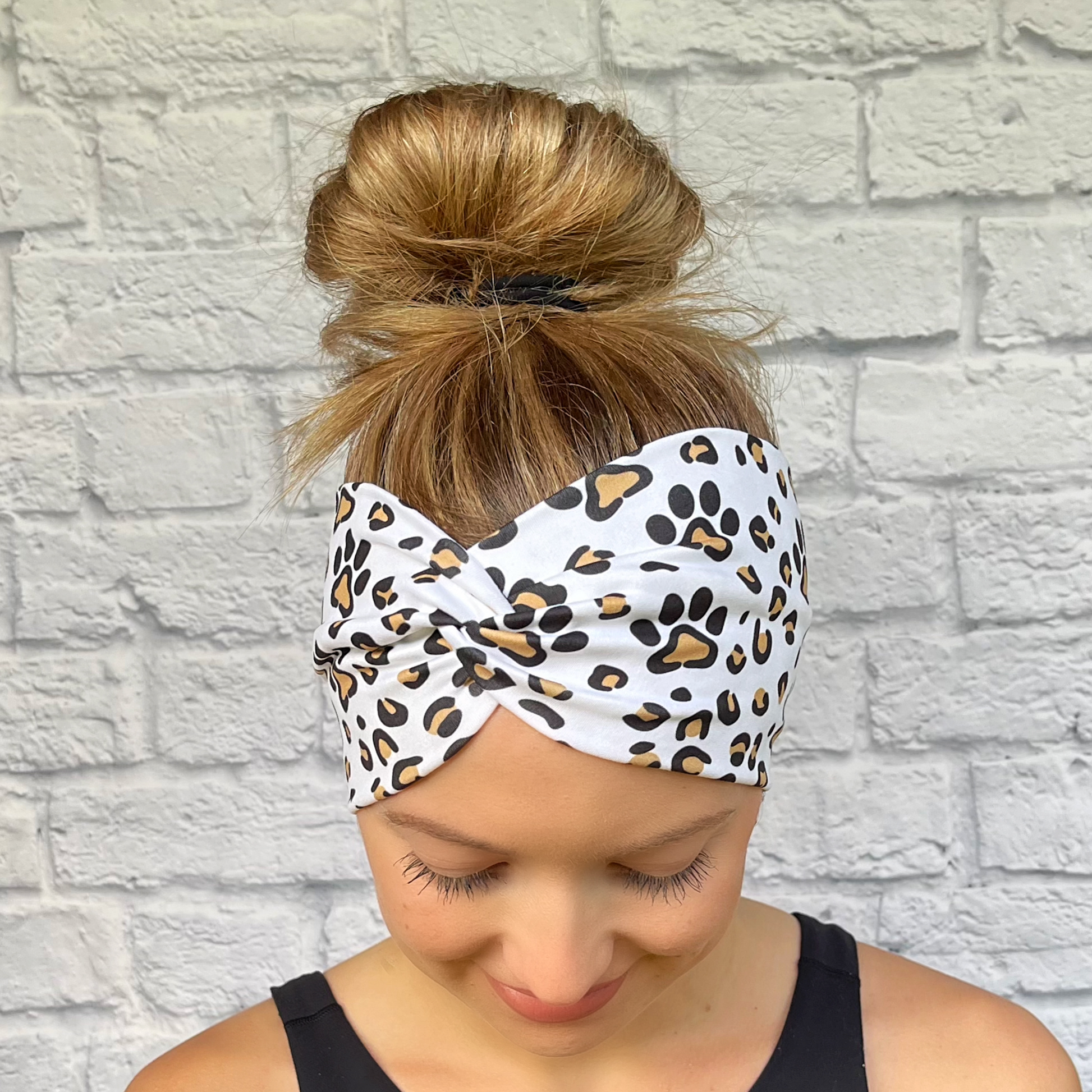 Woman with hair in bun wearing wide, white, twisted headband with brown and black dog paws and cheetah print.
