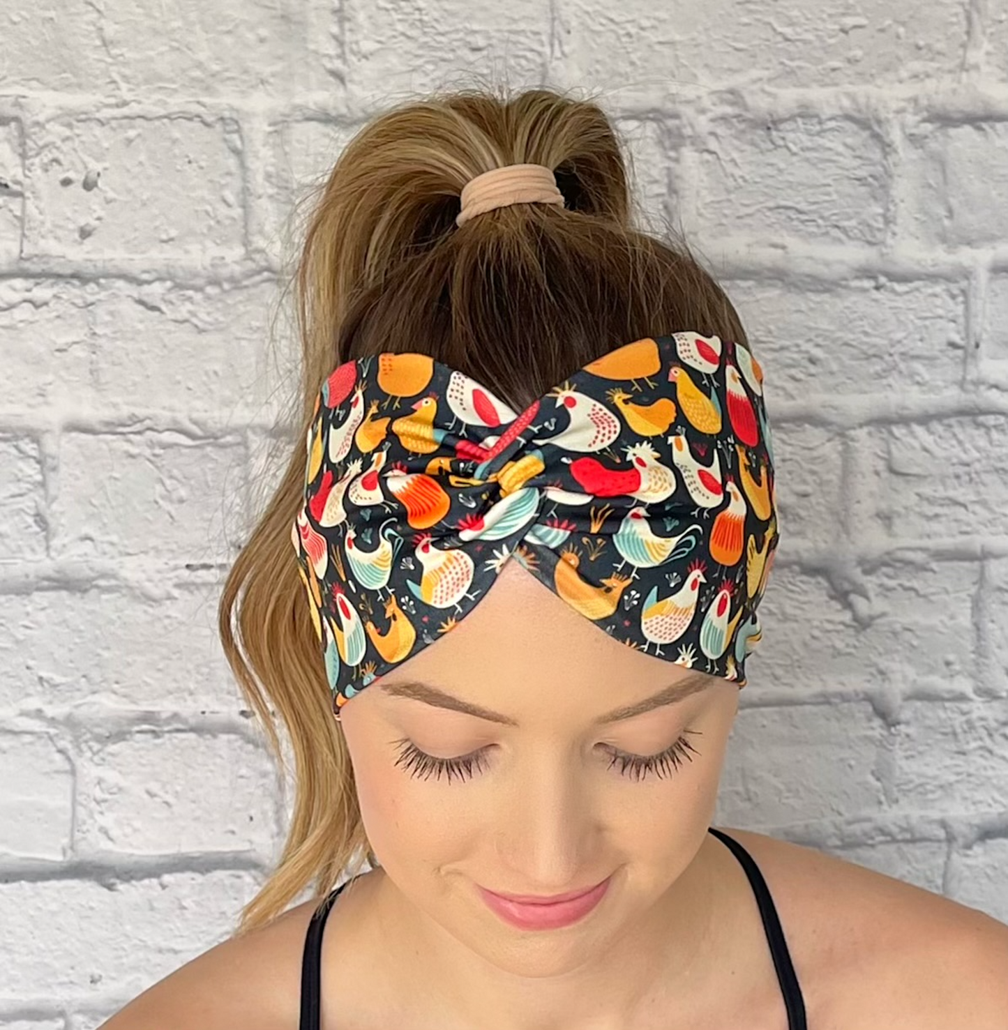 Woman with hair in curled ponytail wearing wide, twisted headband in navy with chicken print.