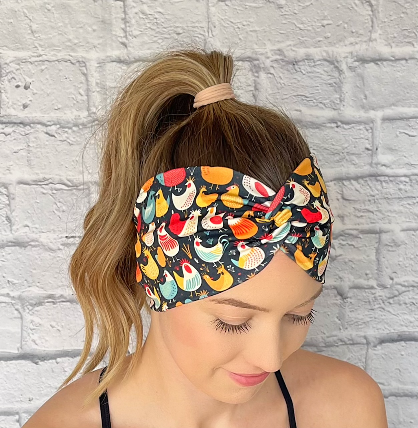 Woman with hair in curled ponytail wearing wide, twisted headband in navy with chicken print.