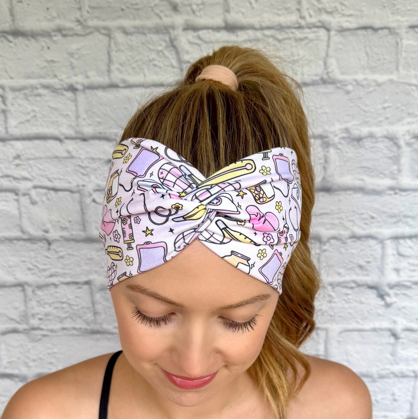 Woman with hair in ponytail wearing wide, twisted headband with yellow, purple, and pink disco and medical theme print.