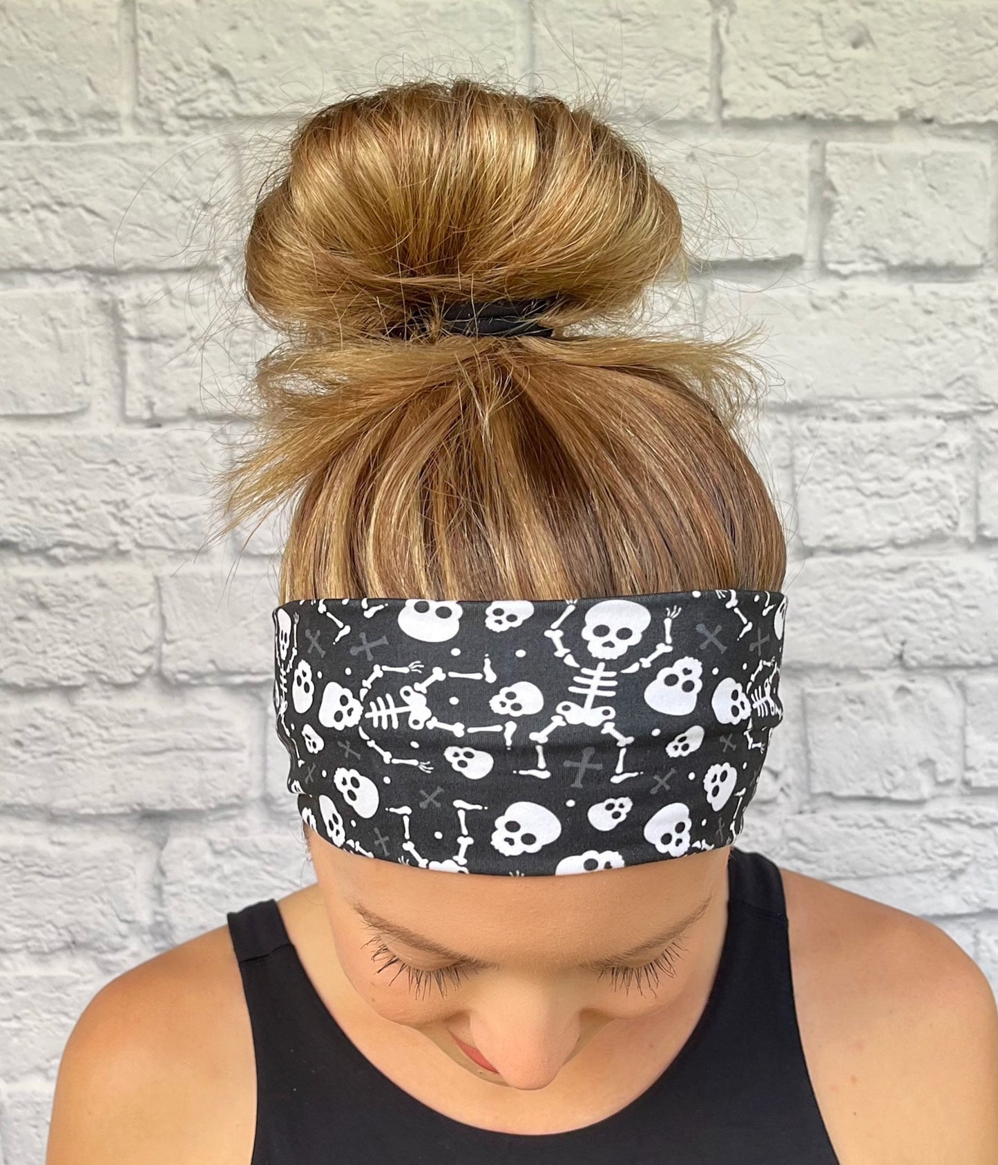 Person wearing a black headband with white skull and skeleton designs against a light gray brick wall.