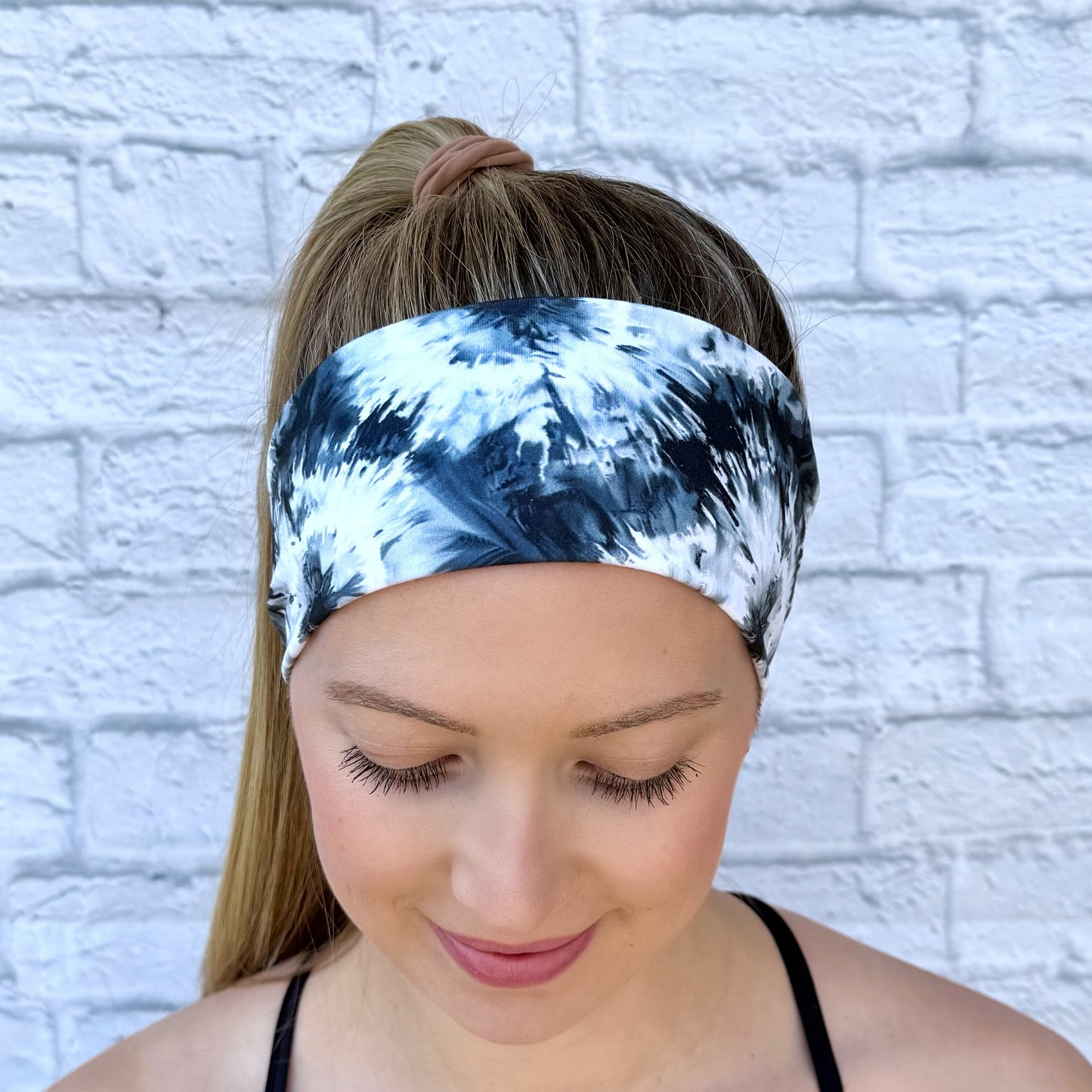 Woman with hair in ponytail wearing flat, stretchy, black and white tie dye headband.