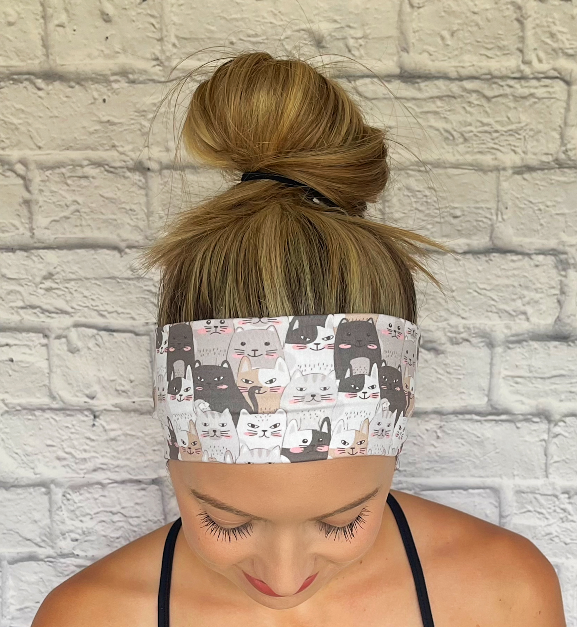 Woman with hair in bun wearing flat, stretchy headband with gray and tan cat print.