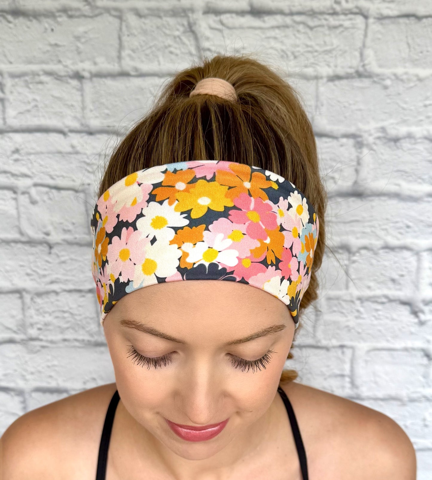 Woman with hair in ponytail wearing headband with light and dark pink, navy, light blue, white, yellow, and orange flower print.