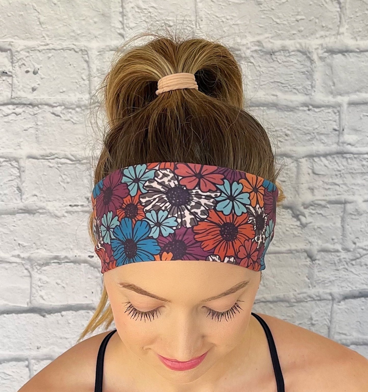 Woman wearing a navy floral headband against a light brick wall.