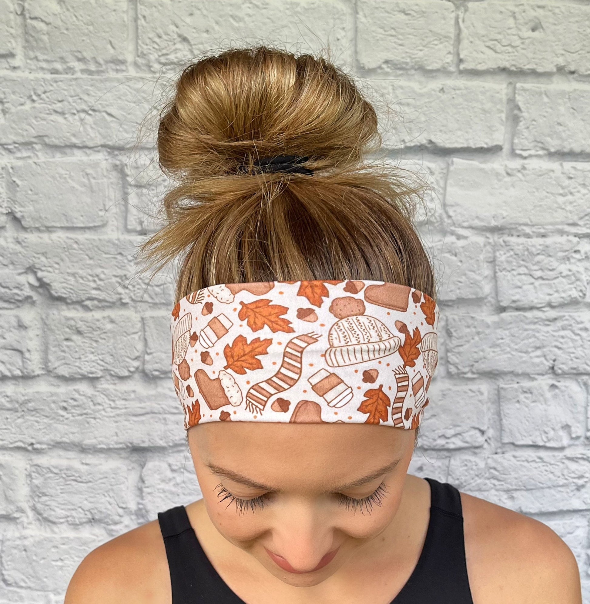 Woman with hair in bun wearing flat, stretchy headband in tan with orange scarves, leaves, hats, coffee, and boots print