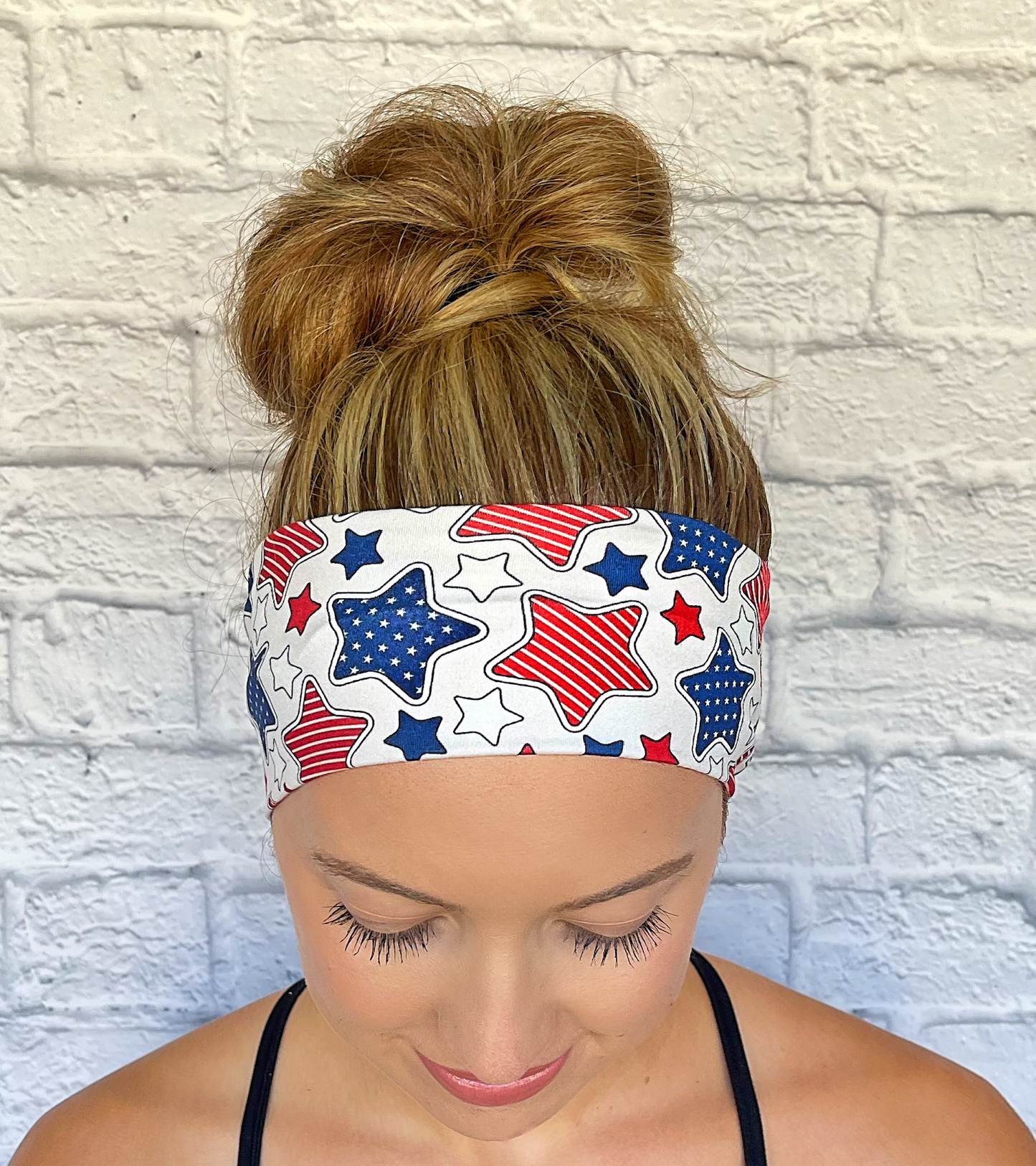 Woman wearing a headband with red, white, and blue star pattern headband against a white brick wall.