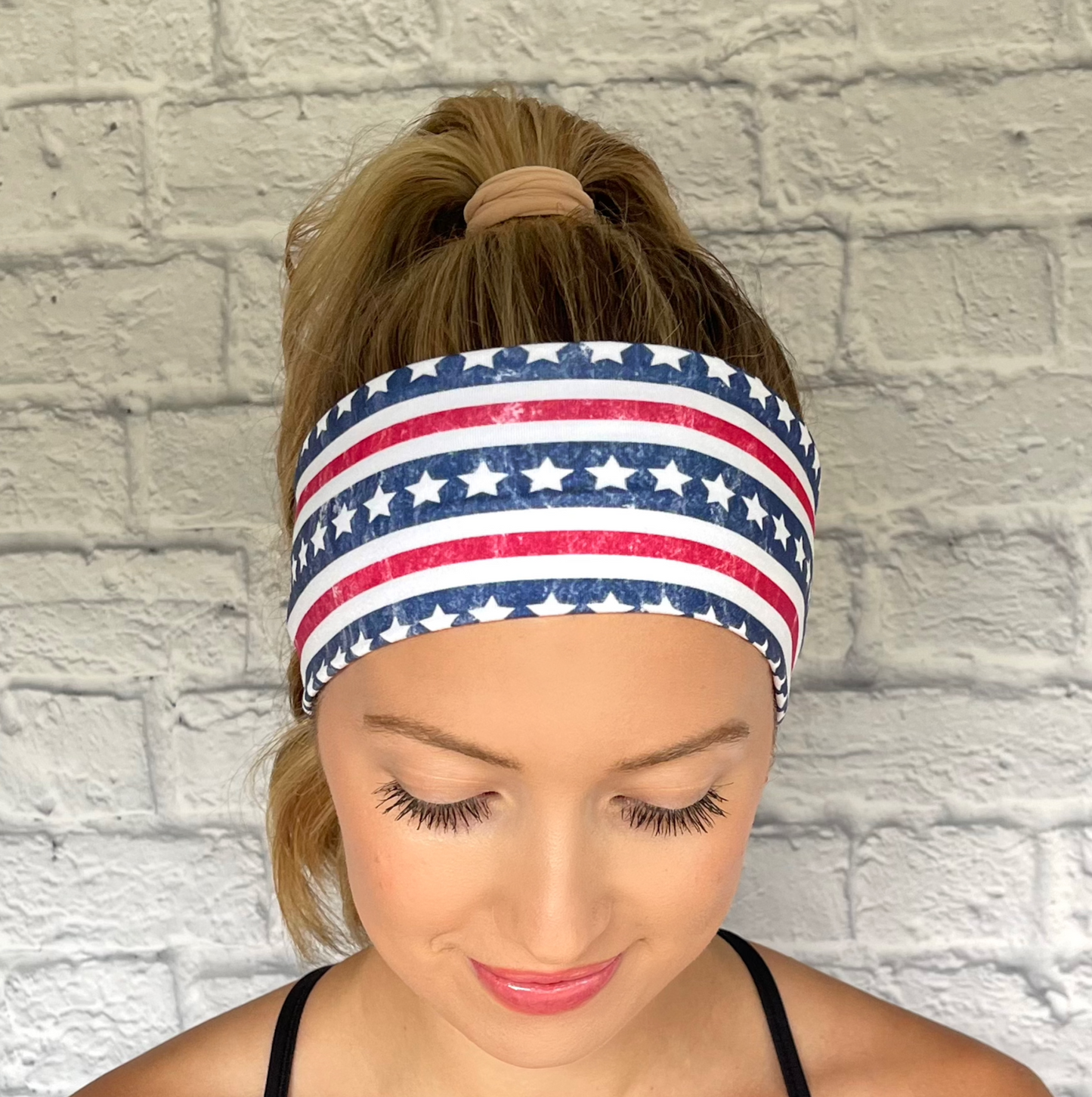 Woman with hair in curled ponytail wearing flat, stretchy headband in USA flag print.