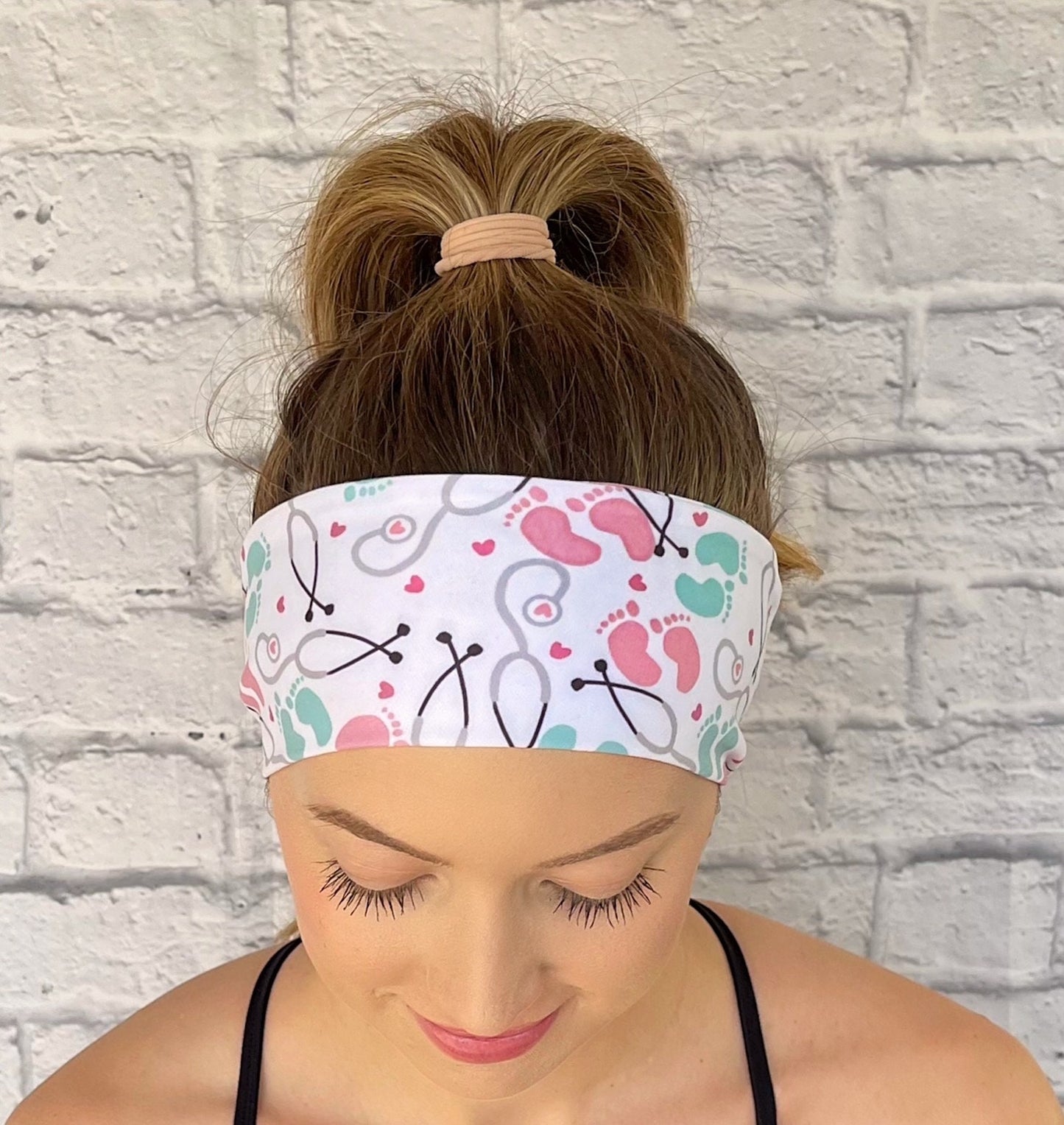 Person wearing a headband with medical-NICU theme headband against a white brick wall.