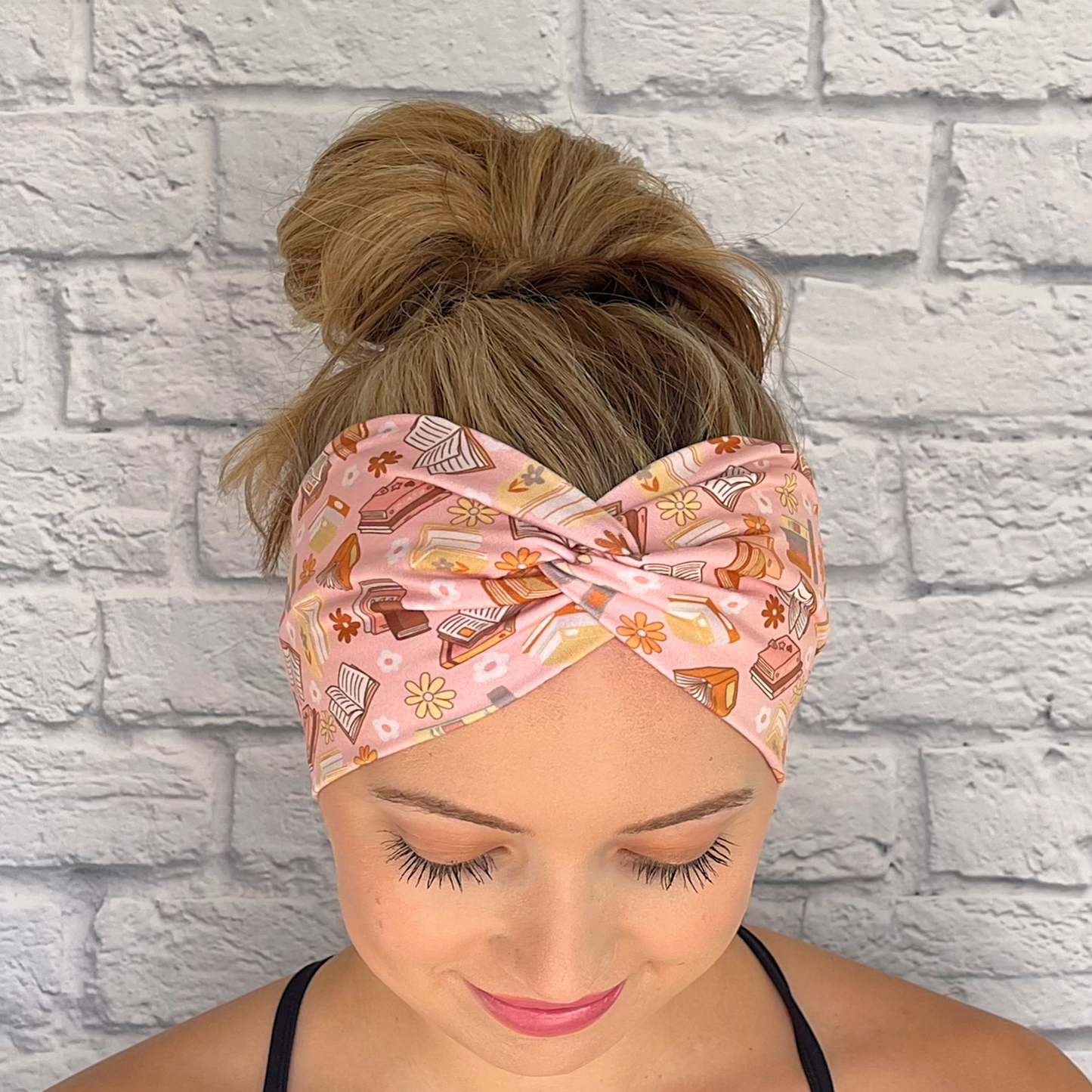 Woman wearing pink, wide twisted headband with books and flower print.