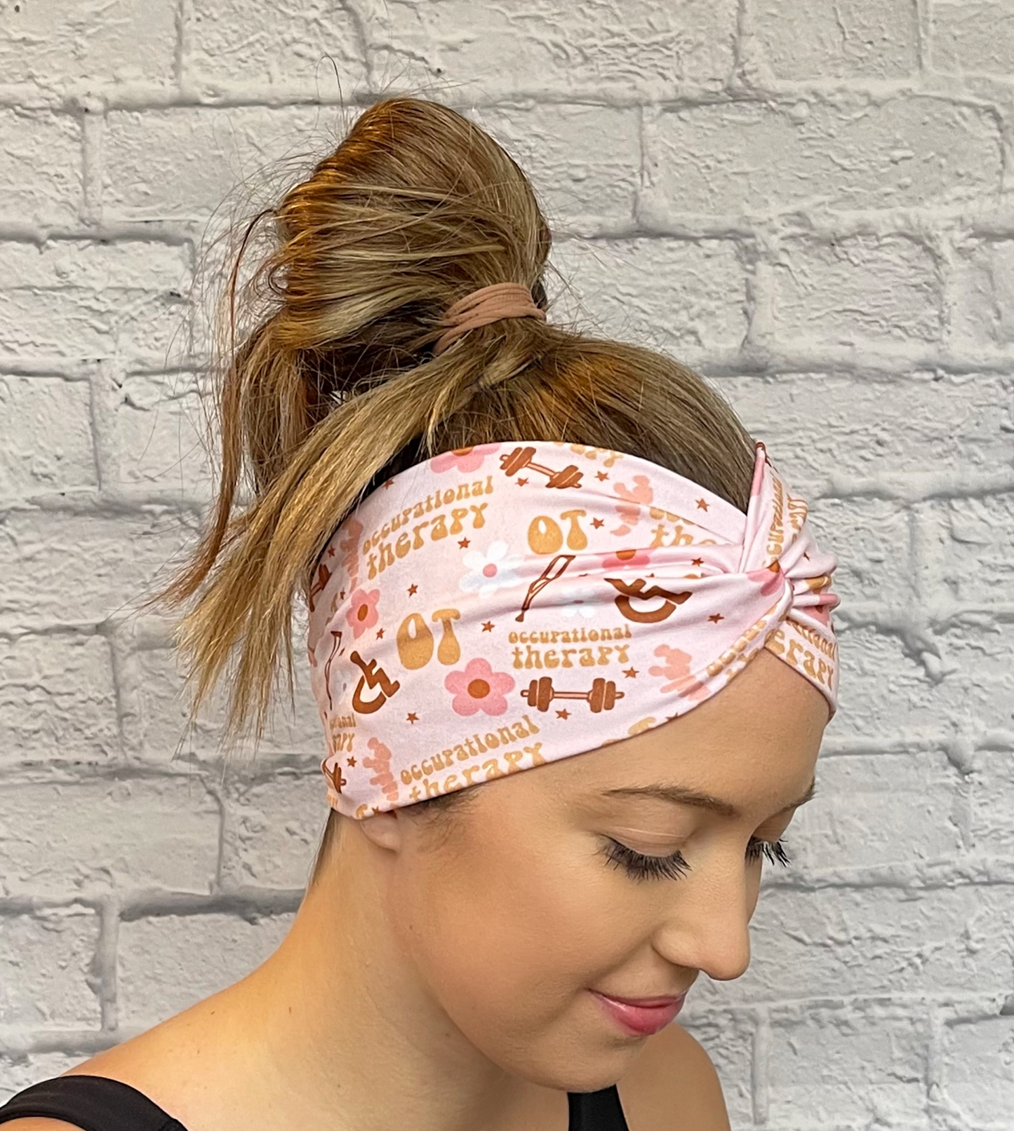Woman with hair in bun wearing wide, twisted, pink headband with print- OT, occupational therapy with flowers, crutches, a wheelchair, and weights.