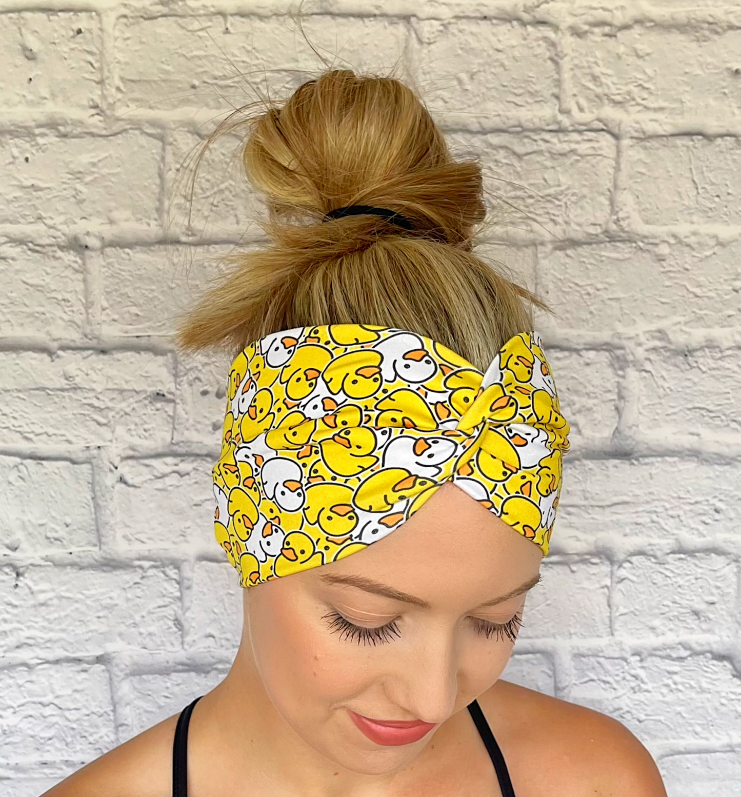 Woman with hair in bun wearing wide, twisted headband in yellow and white rubber duck print.