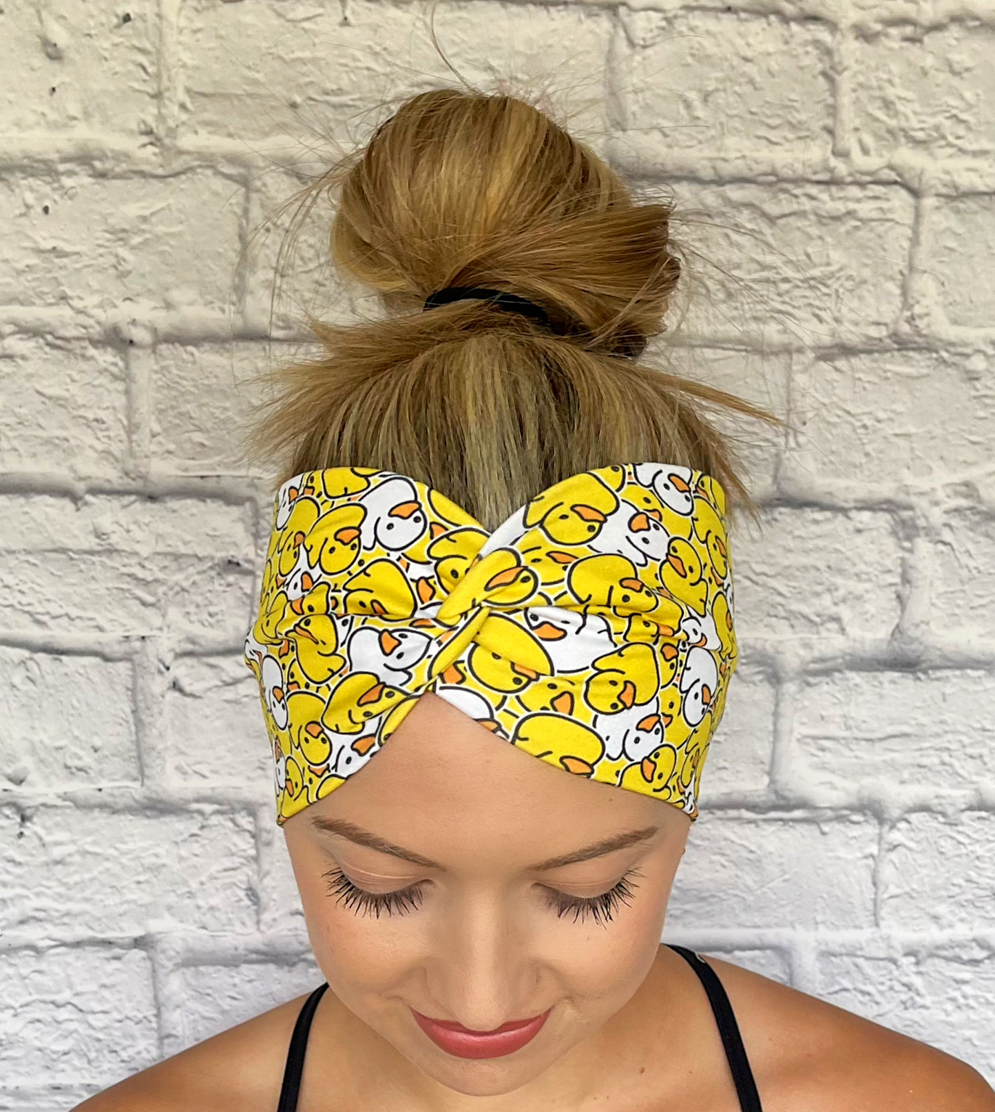 Woman with hair in bun wearing wide, twisted headband in yellow and white rubber duck print.