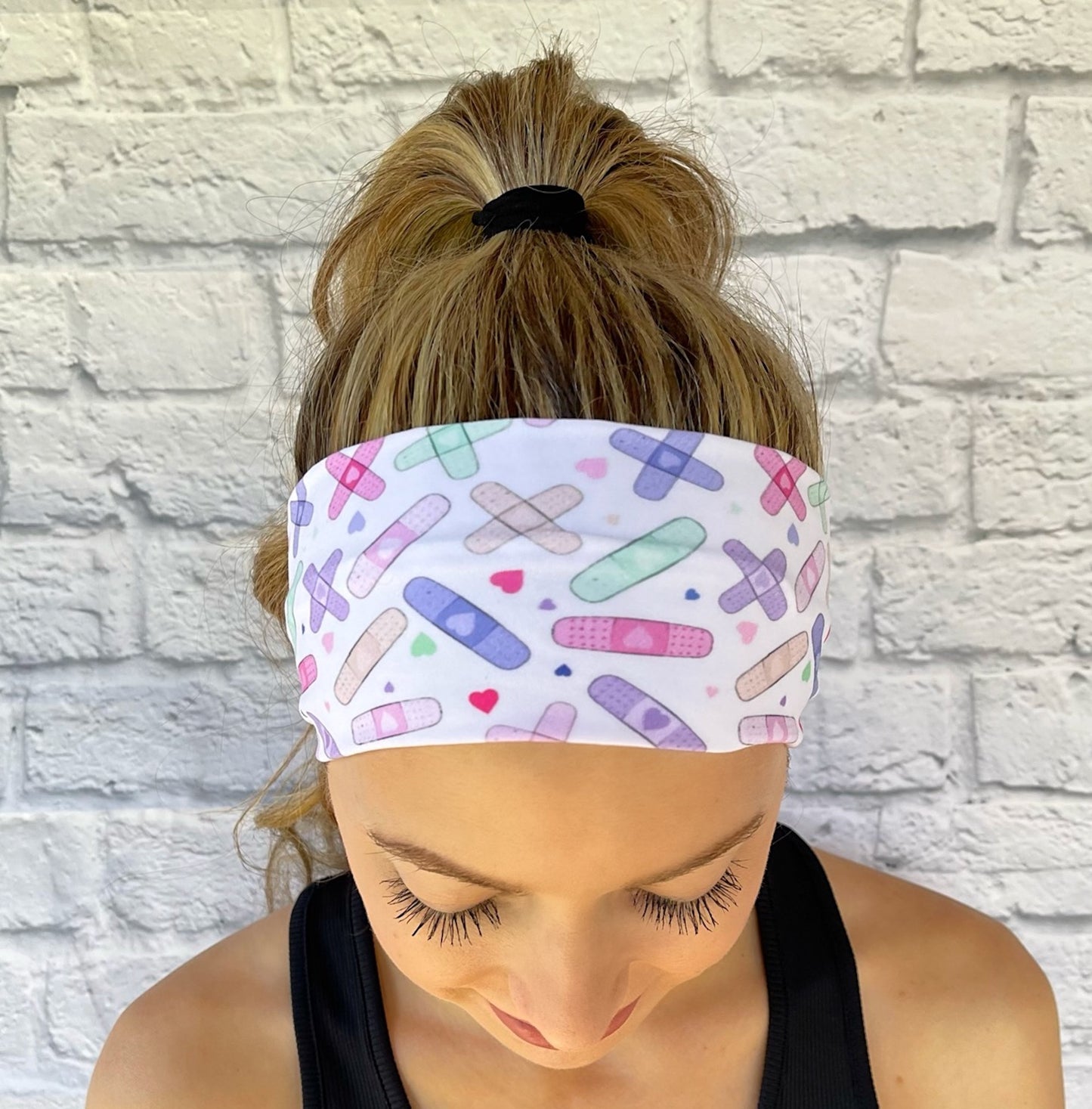 Woman with hair in curled ponytail wearing white, stretchy headband with pastel color bandages print.
