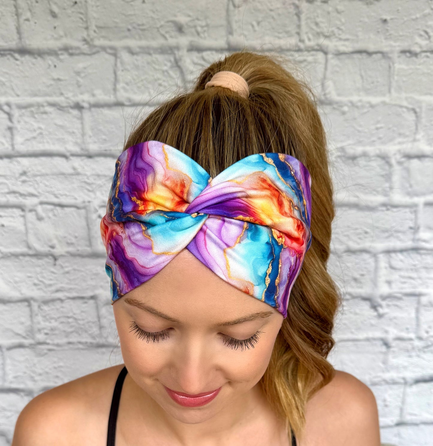 Woman with hair in ponytail wearing wide, twisted headband in multi-color watercolor print.
