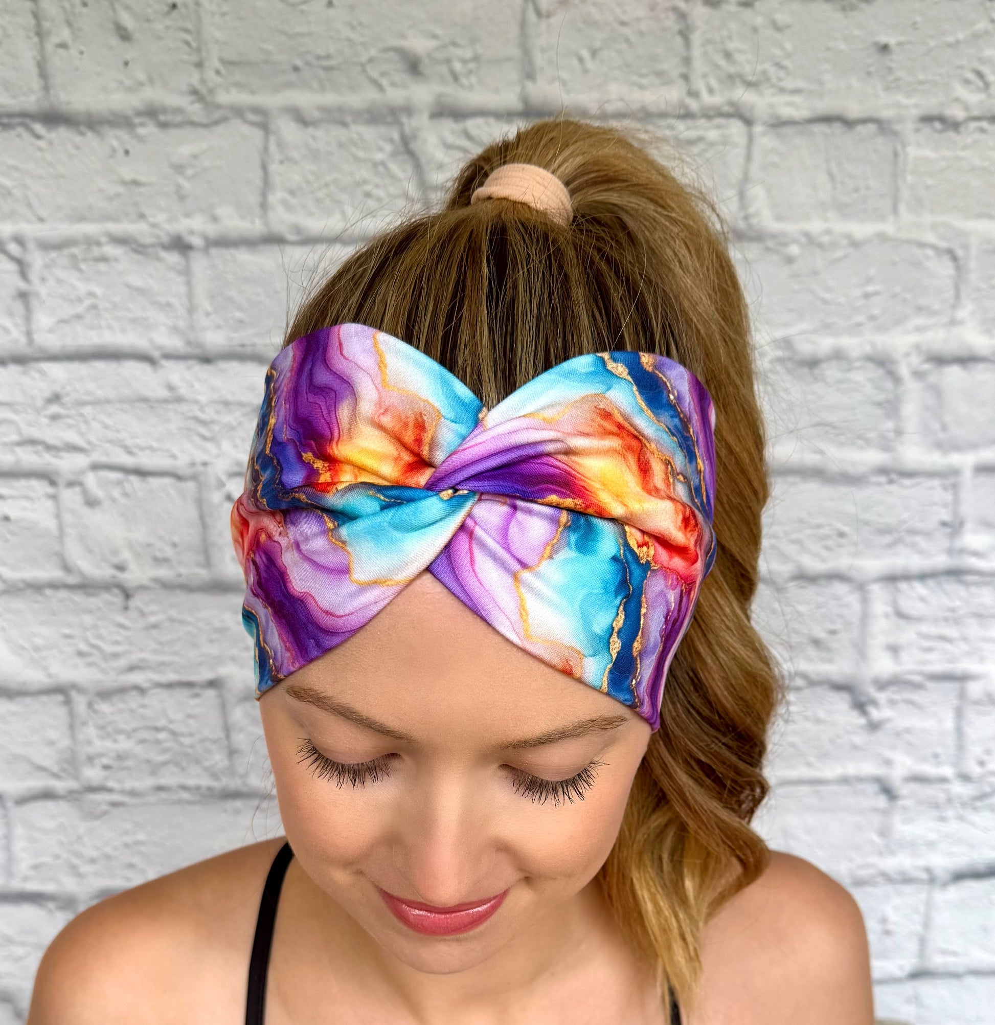 Woman with hair in ponytail wearing wide, twisted headband in multi-color watercolor print.