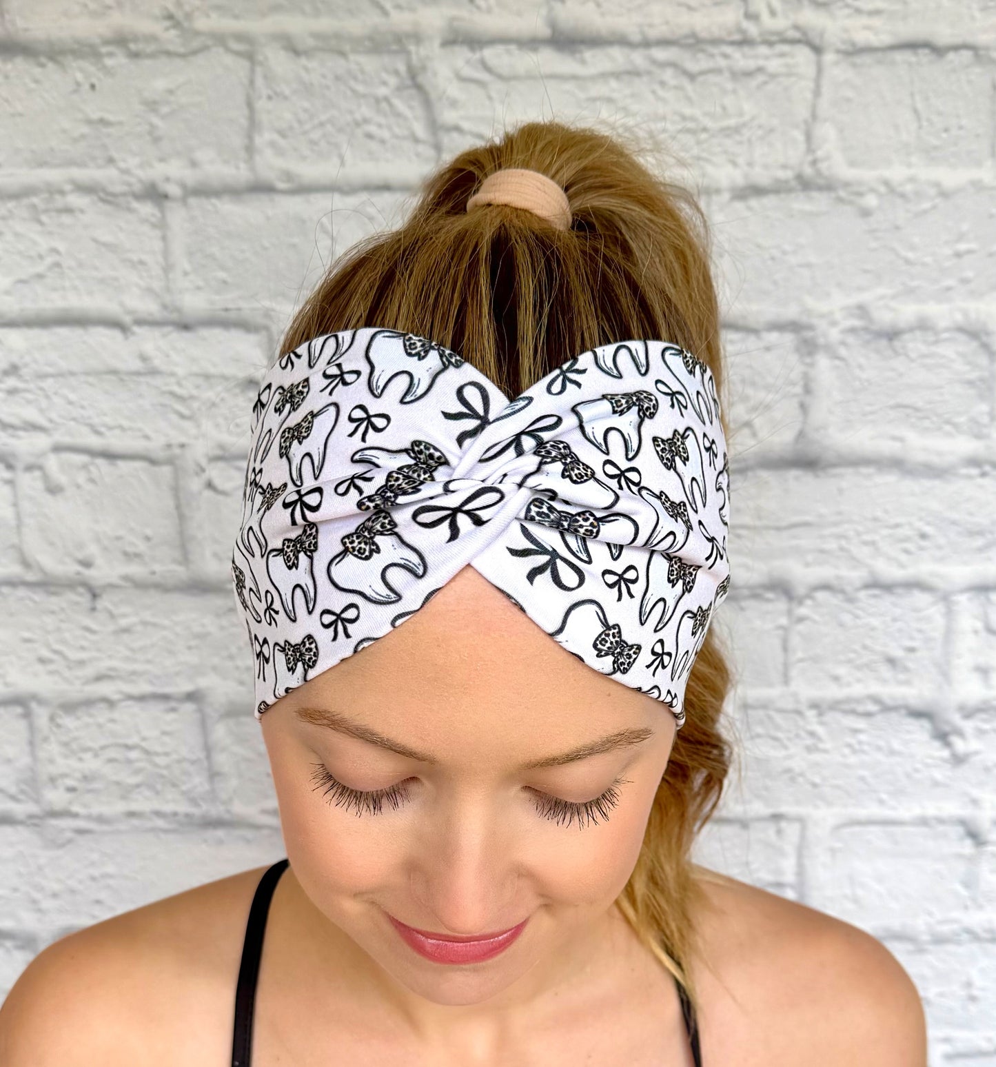 Woman with hair in curled ponytail wearing wide, twisted, white headband in white with teeth and bow print in black and cheetah print.