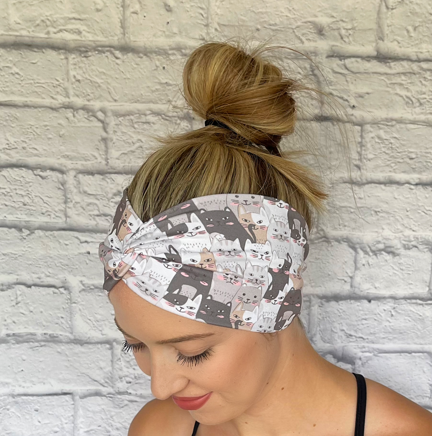 Woman with hair in bun wearing wide, twisted headband in with gray and tan cat print.