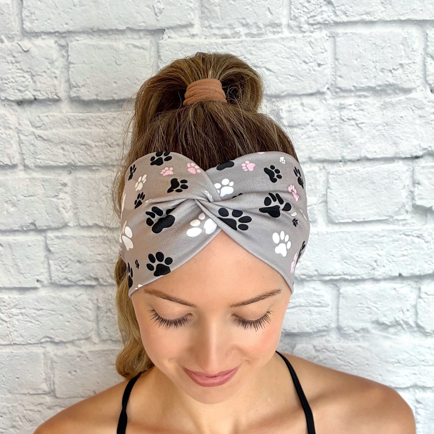 Woman with hair in ponytail wearing wide, twisted, gray headband with pink, black, and white dog paw print.
