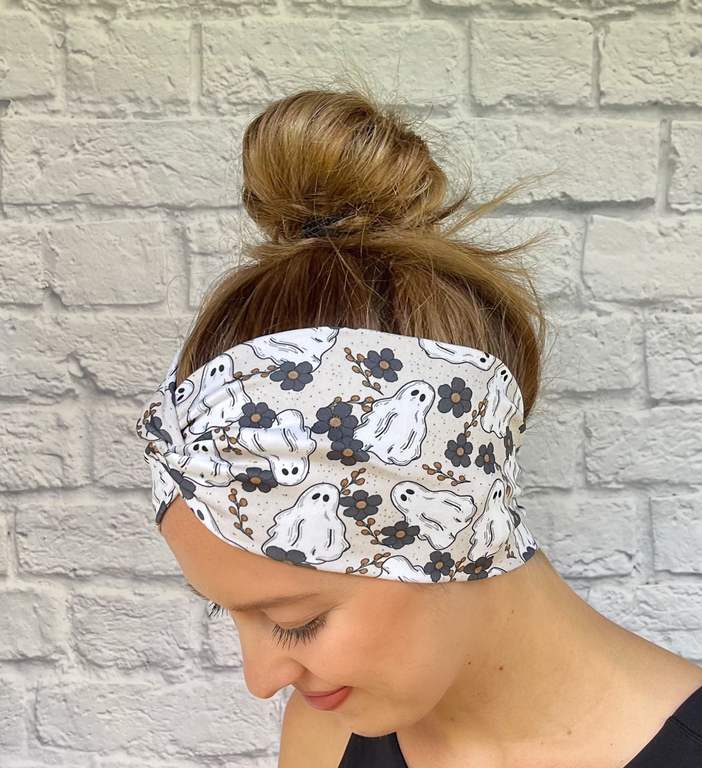 Woman with hair in bun wearing wide, twisted headband in cream/gray with floral and ghost print.