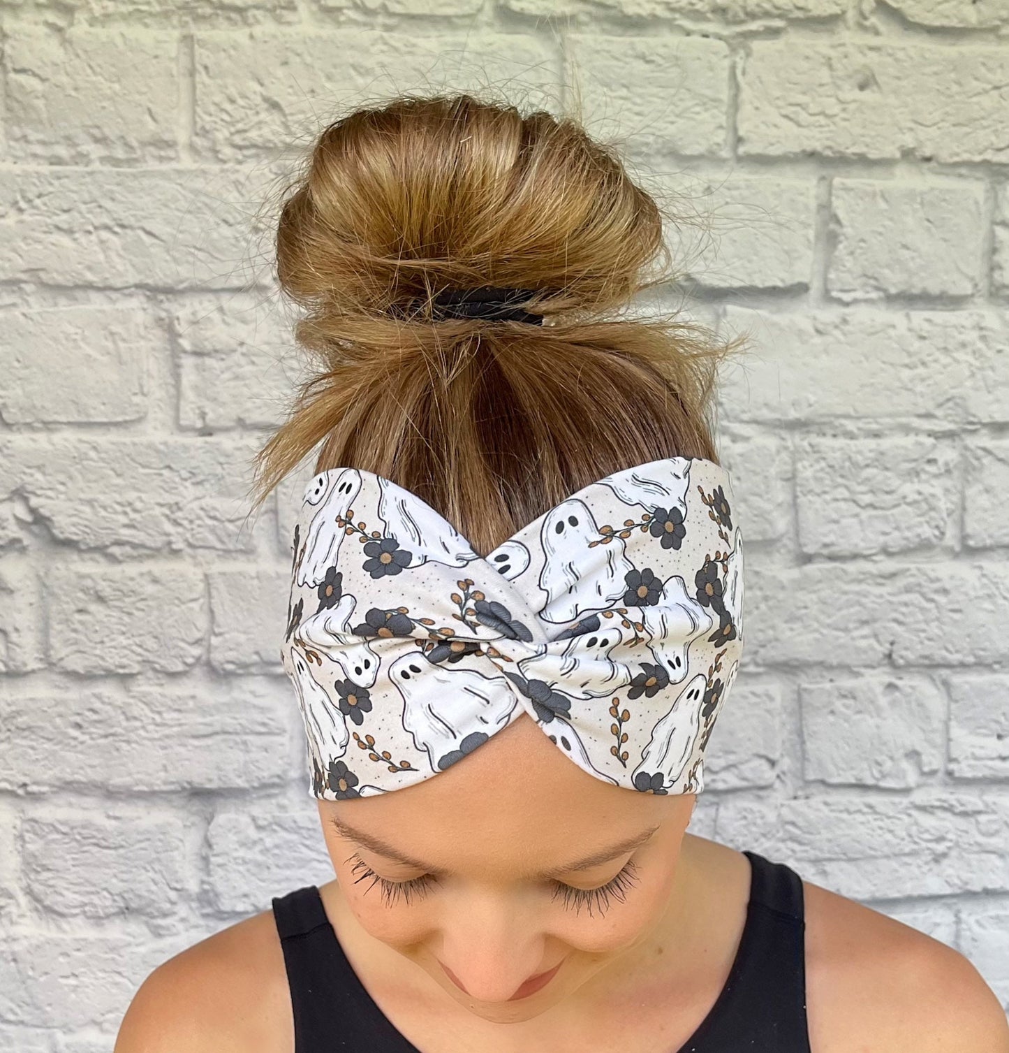 Woman with hair in bun wearing wide, twisted headband in cream/gray with floral and ghost print.