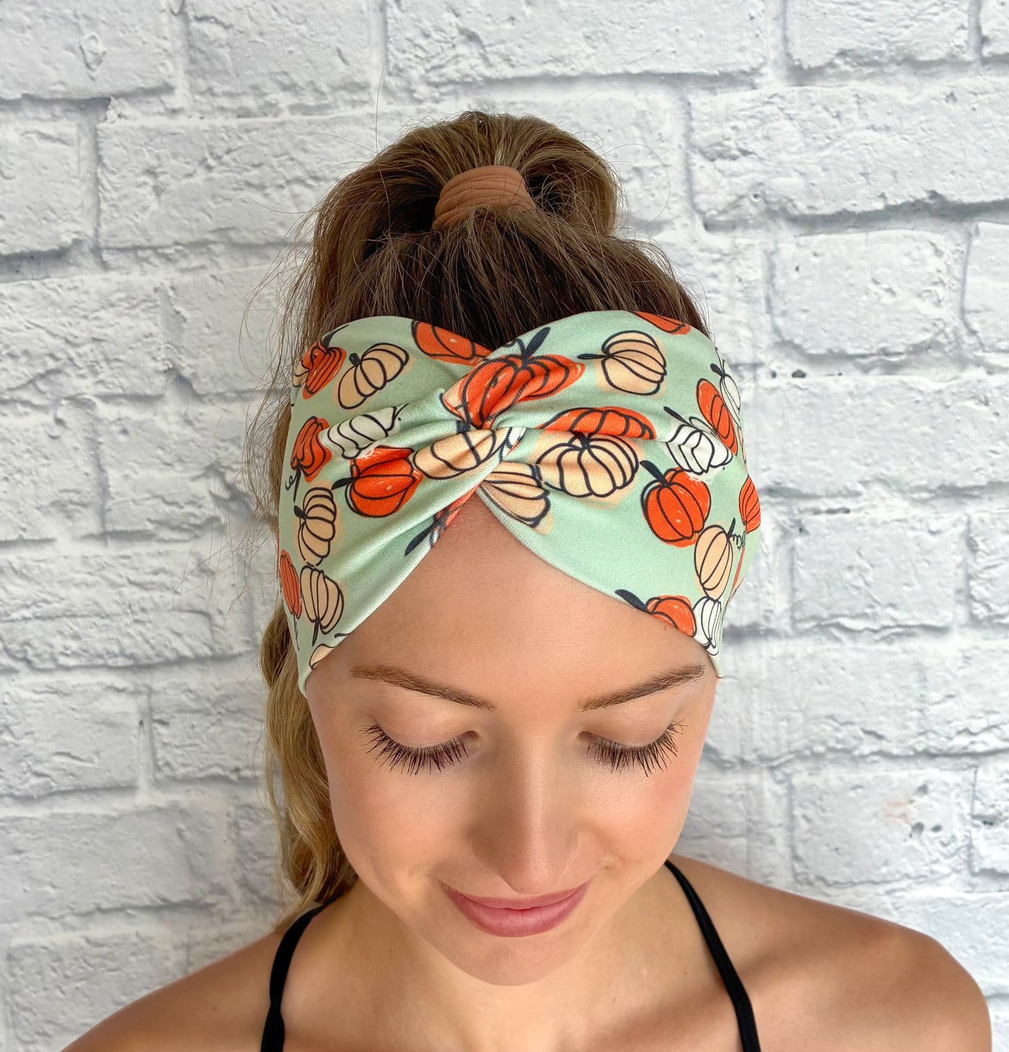 Woman with hair in ponytail wearing wide, twisted, stretchy, mint green headband with pumpkin print.