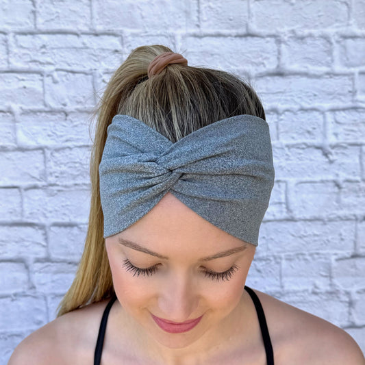 Woman with hair in ponytail wearing wide, stretchy, twisted, heather gray color headband.
