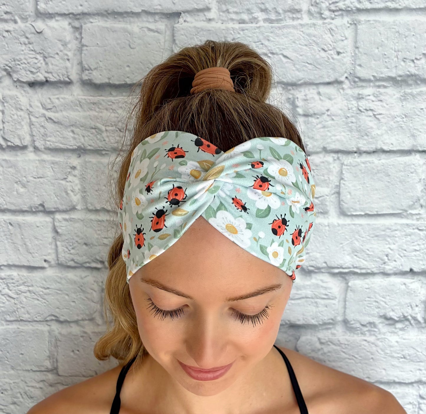 Woman wearing a headband with ladybug pattern against a white brick wall.